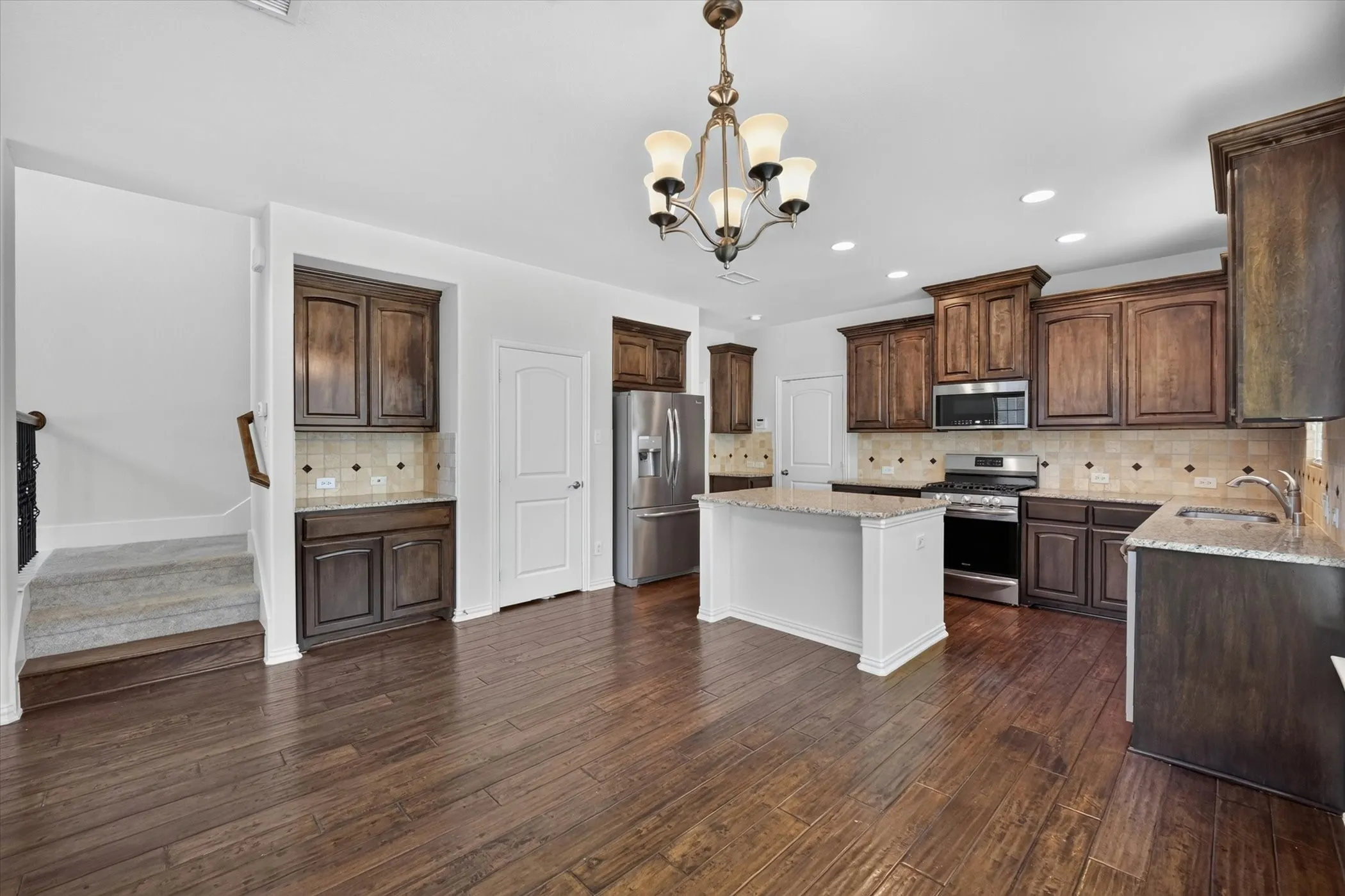 Open concept kitchen featuring dark wood cabinetry, stainless steel appliances, a central island with countertop, and wood-finish flooring