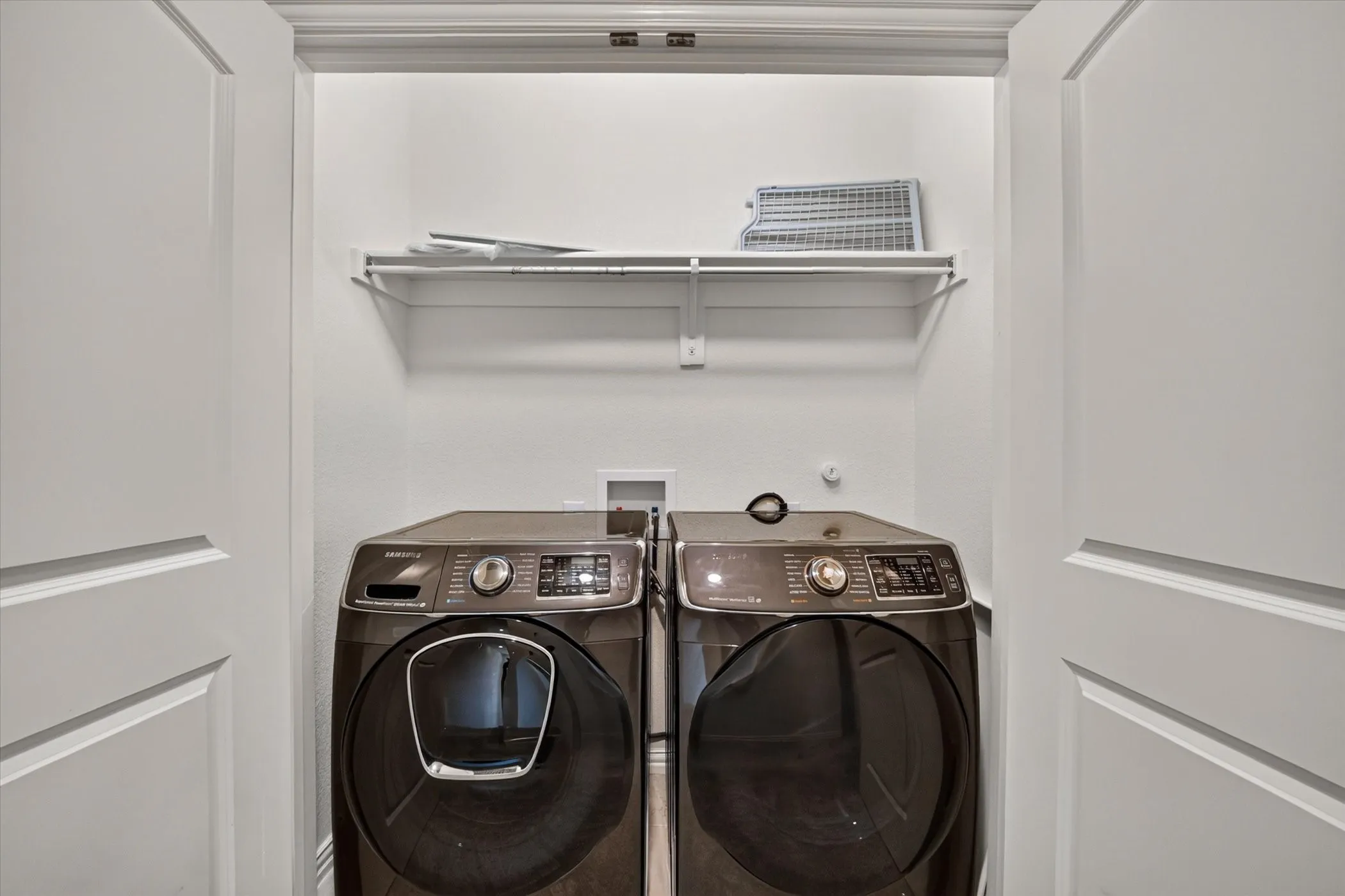 Laundry closet featuring white bi-fold doors, white interior walls, and a single white wire shelf