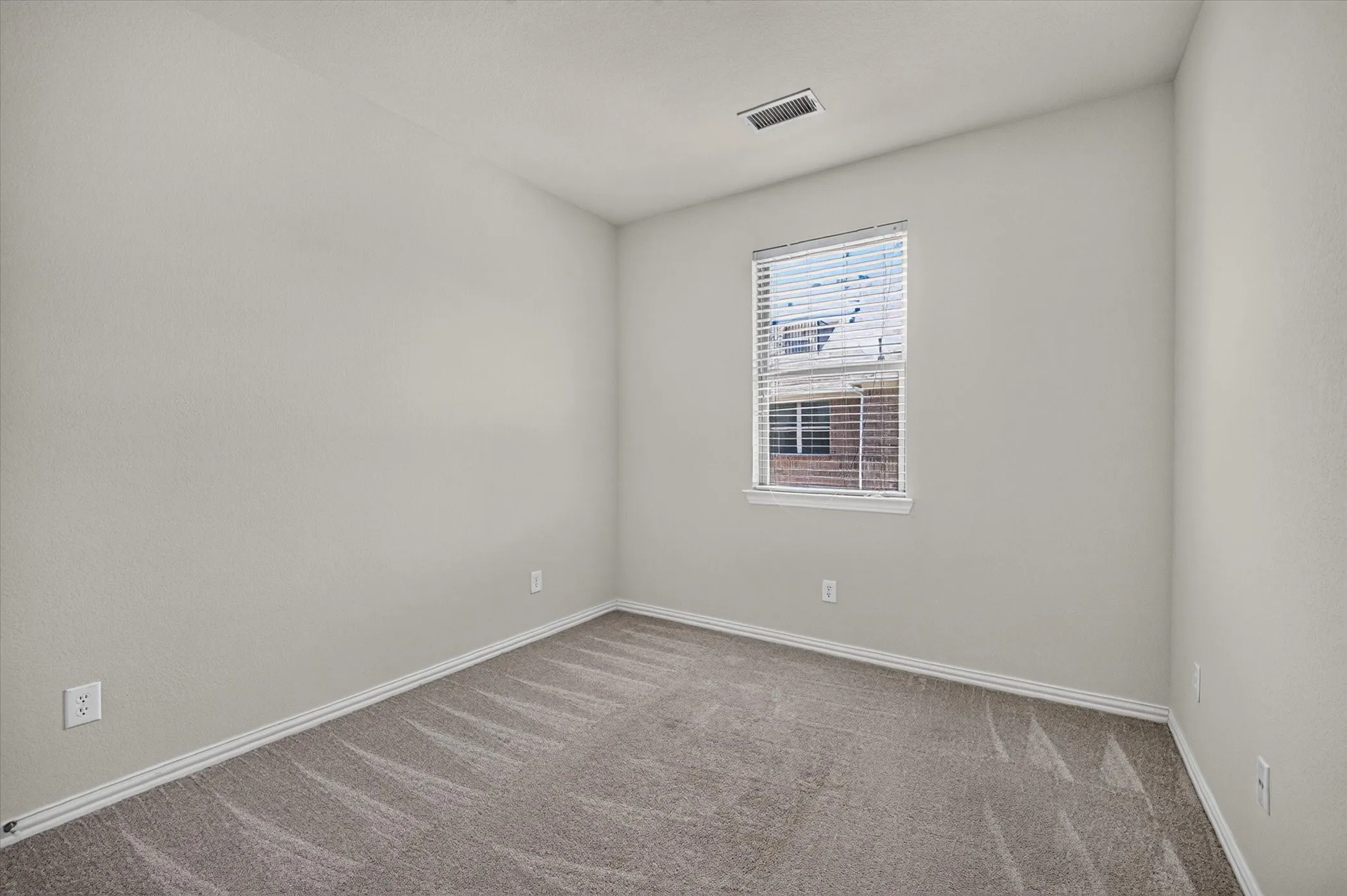 Spacious room featuring light gray walls, plush patterned carpeting, and white baseboards