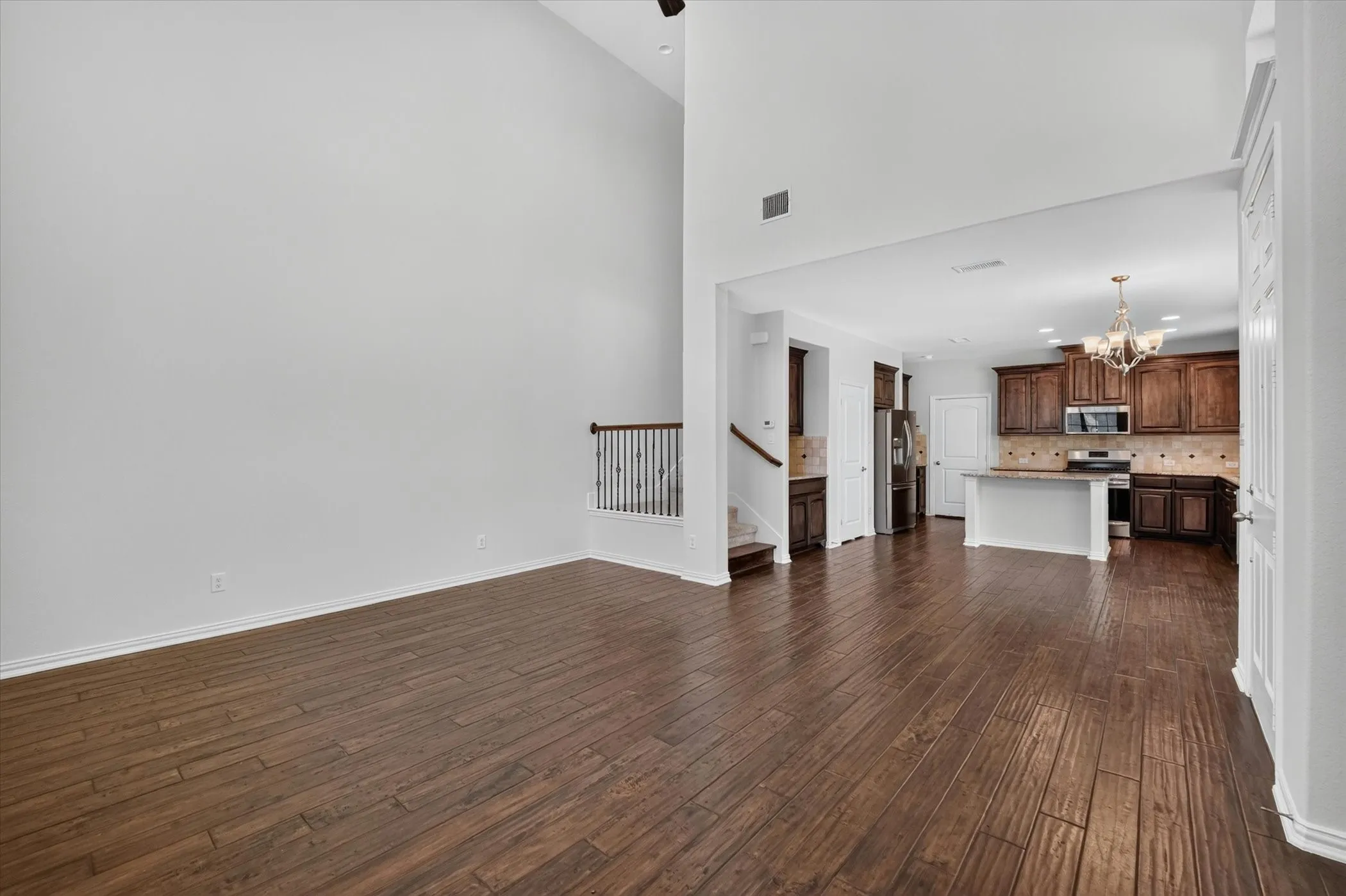 Two-story living area featuring wood-finish flooring, a contemporary staircase with iron balusters, and a kitchen with dark wood cabinetry