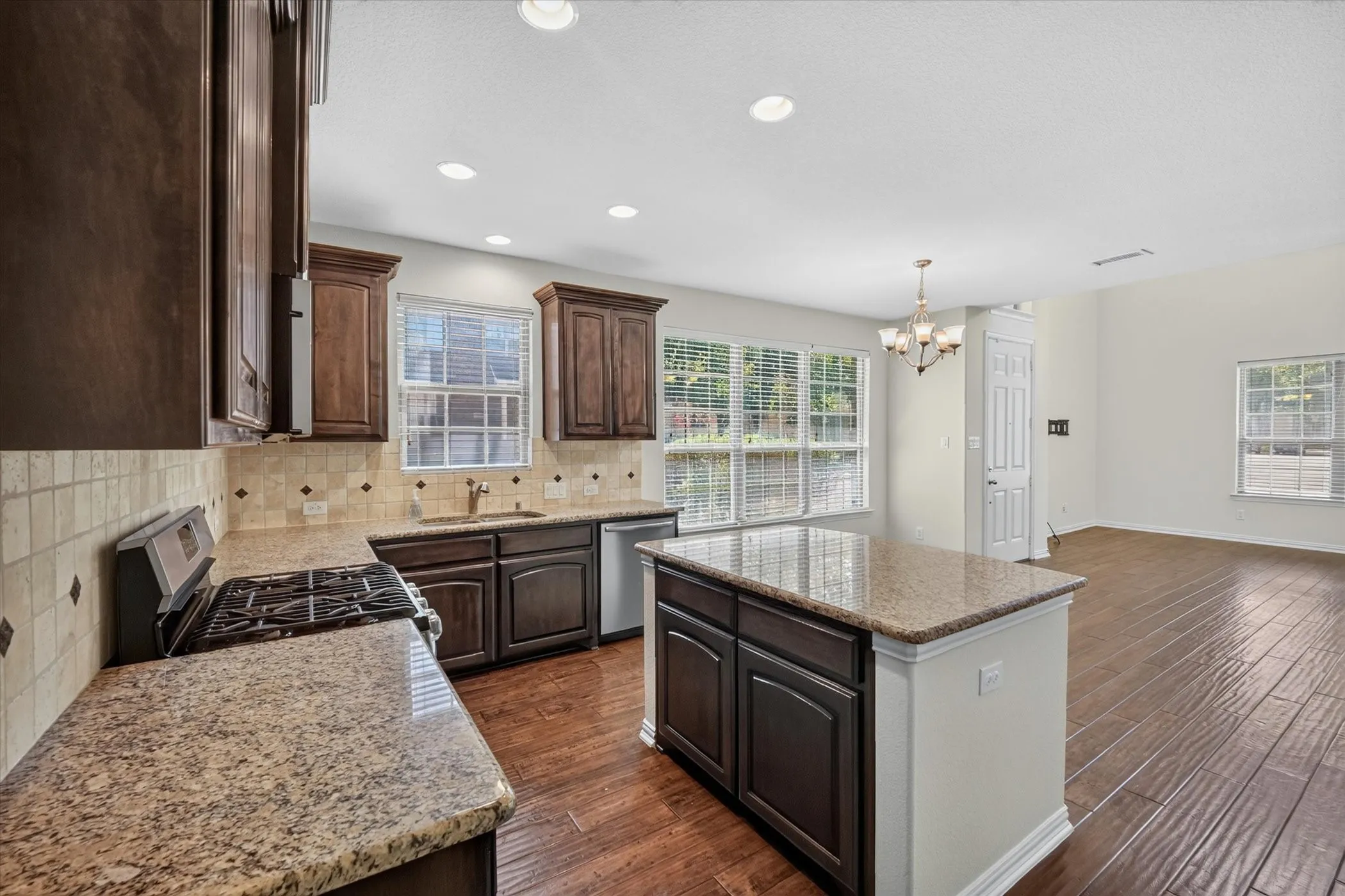 Kitchen featuring dark wood cabinetry, granite countertops, tile backsplash with accent inserts, a central island, and recessed lighting