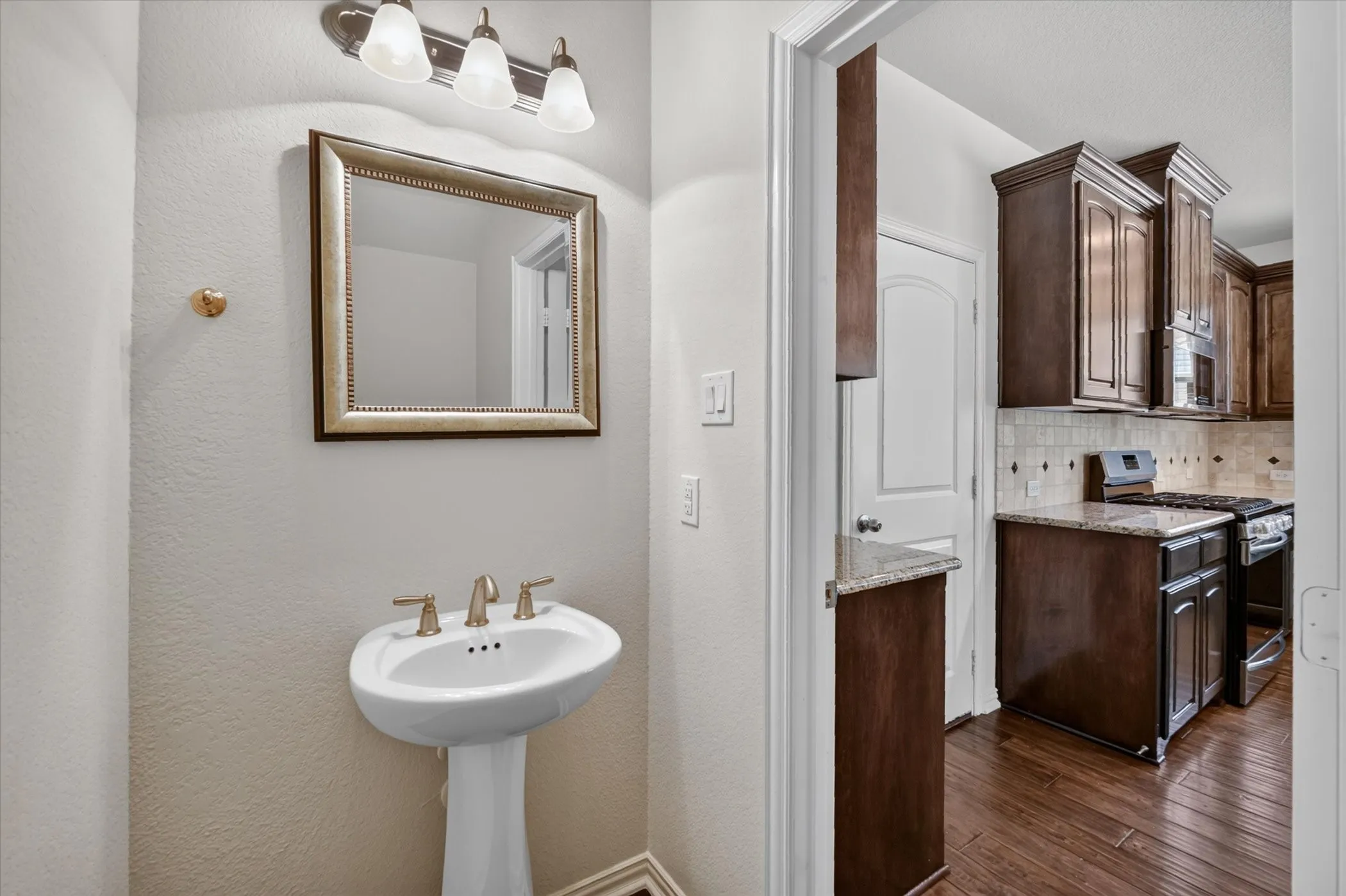 Pedestal sink with brass-finish faucet, framed mirror, and three-light vanity fixture