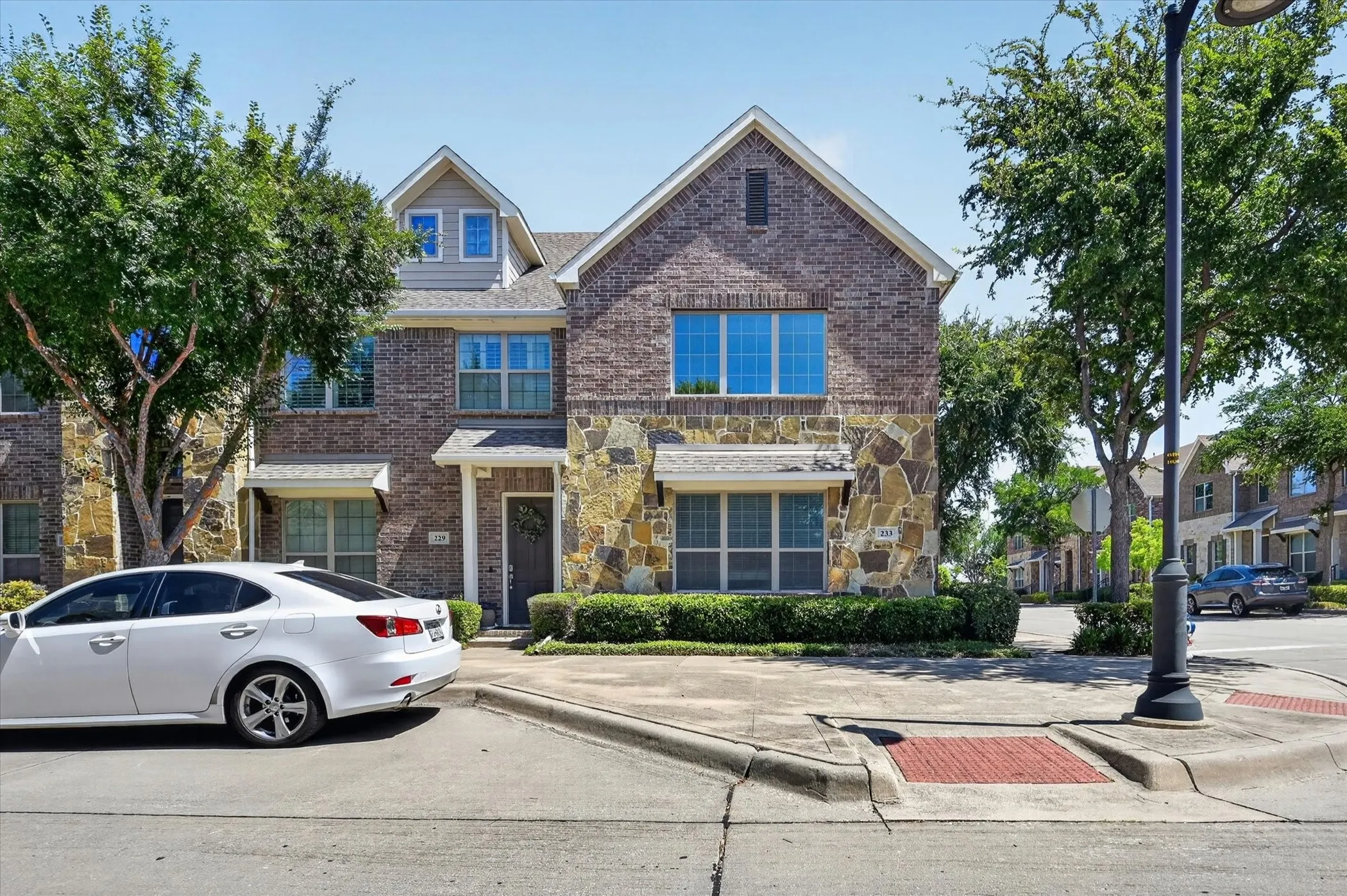 Multi-story residence featuring brick and stone exterior finishes, dormer windows, and mature trees
