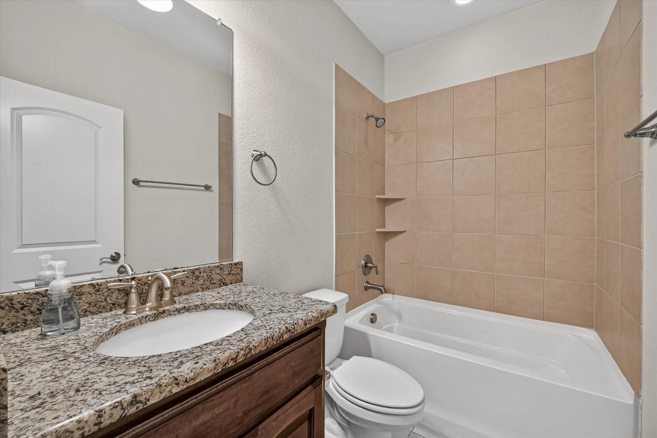 Bathroom featuring a white bathtub, tiled shower surround with built-in shelves, single vanity with a granite countertop, and a large wall mirror