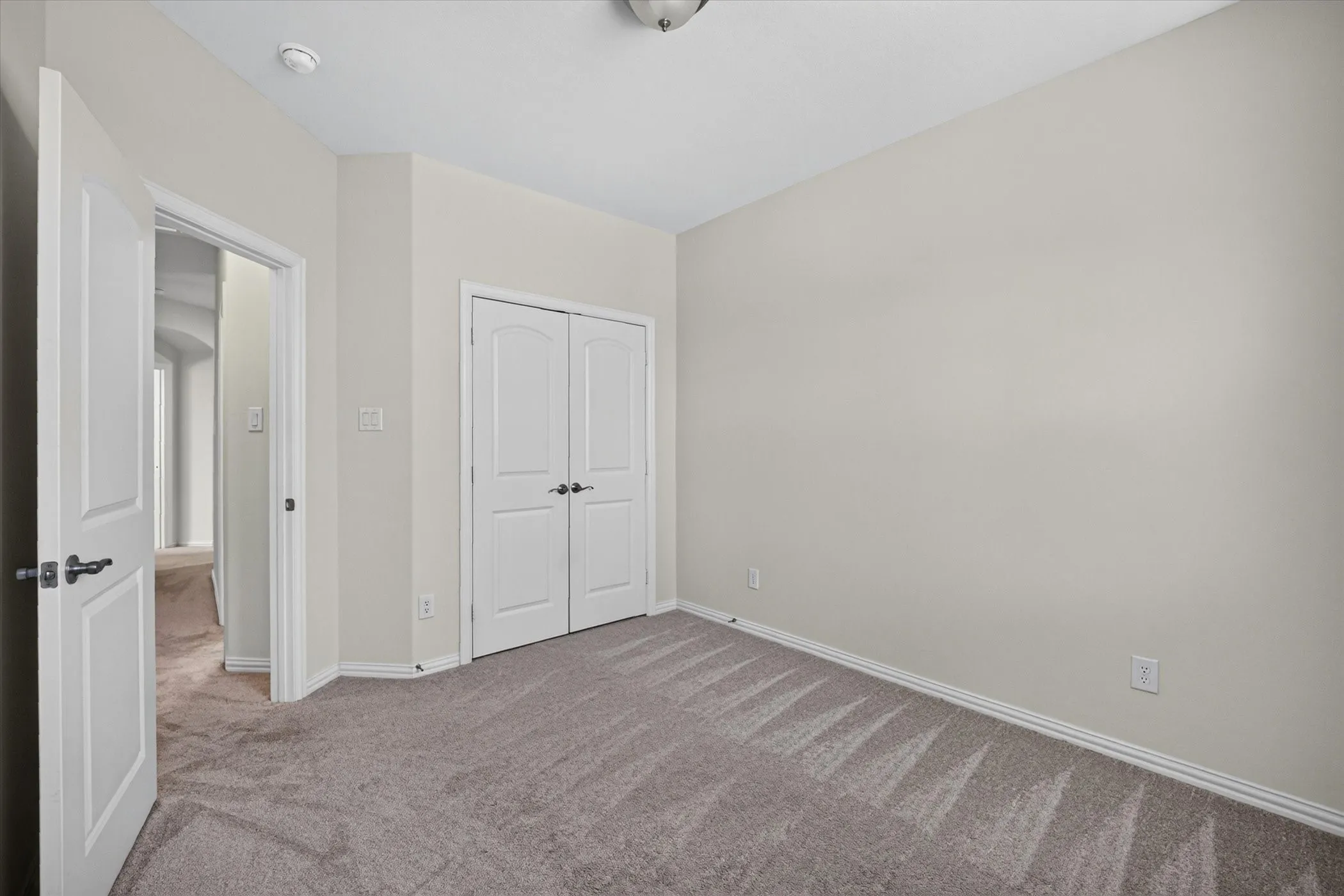 Room featuring light-toned walls, gray carpet flooring, white baseboards, and a double-door closet with dark hardware