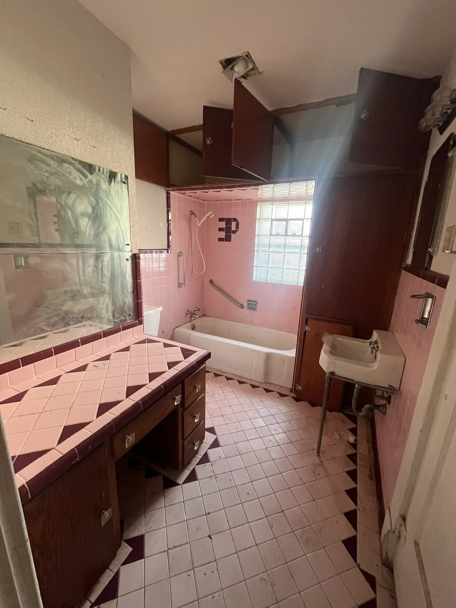 Bathroom featuring a built-in vanity with tiled countertop, full bathtub, and glass block window