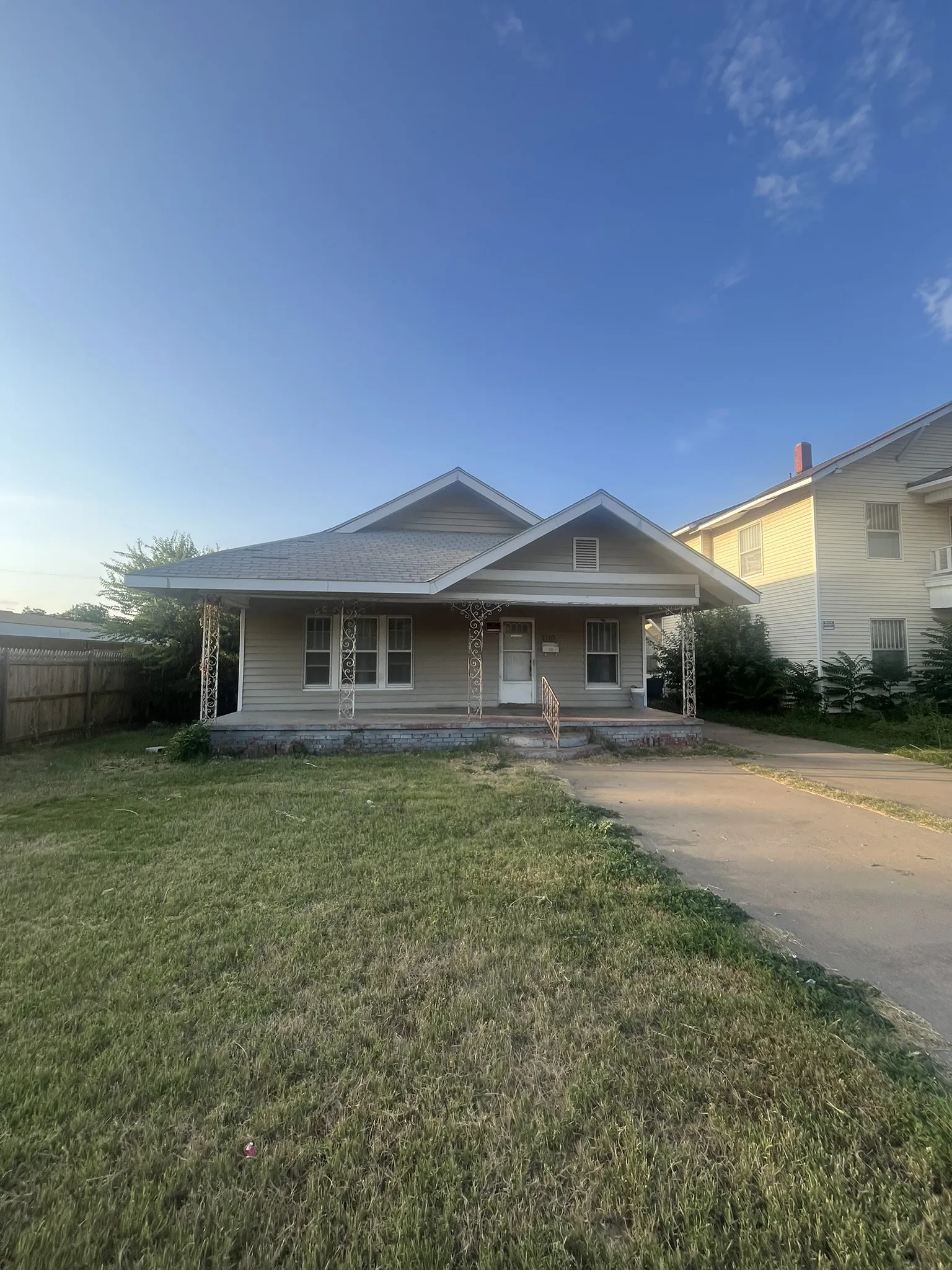 Single-story residence featuring light-colored siding, a covered front porch with decorative metal columns, and a gabled roofline