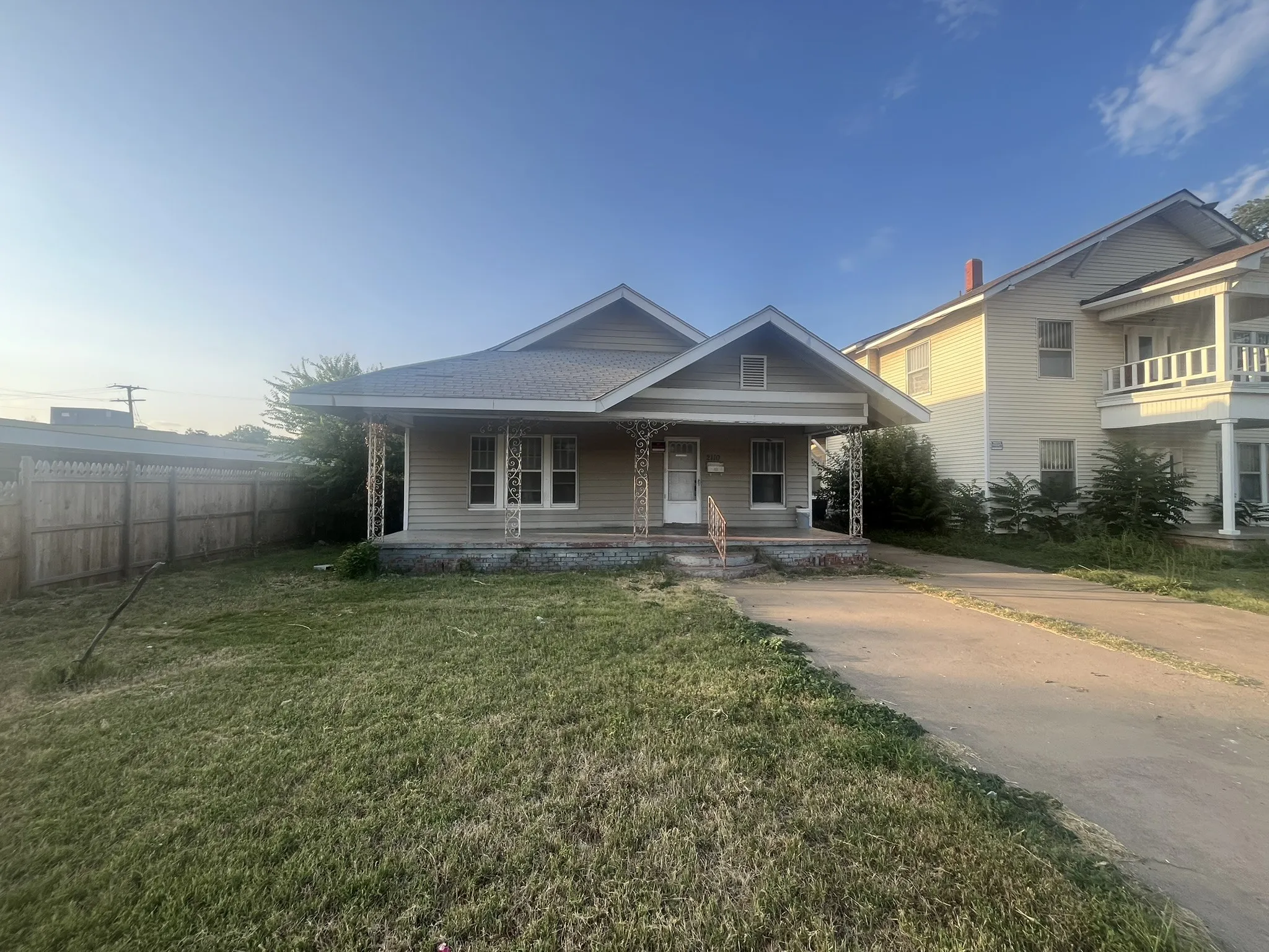 Single-story residence featuring light-colored siding, a covered front porch with decorative metal columns, a gabled roofline, and a paved driveway