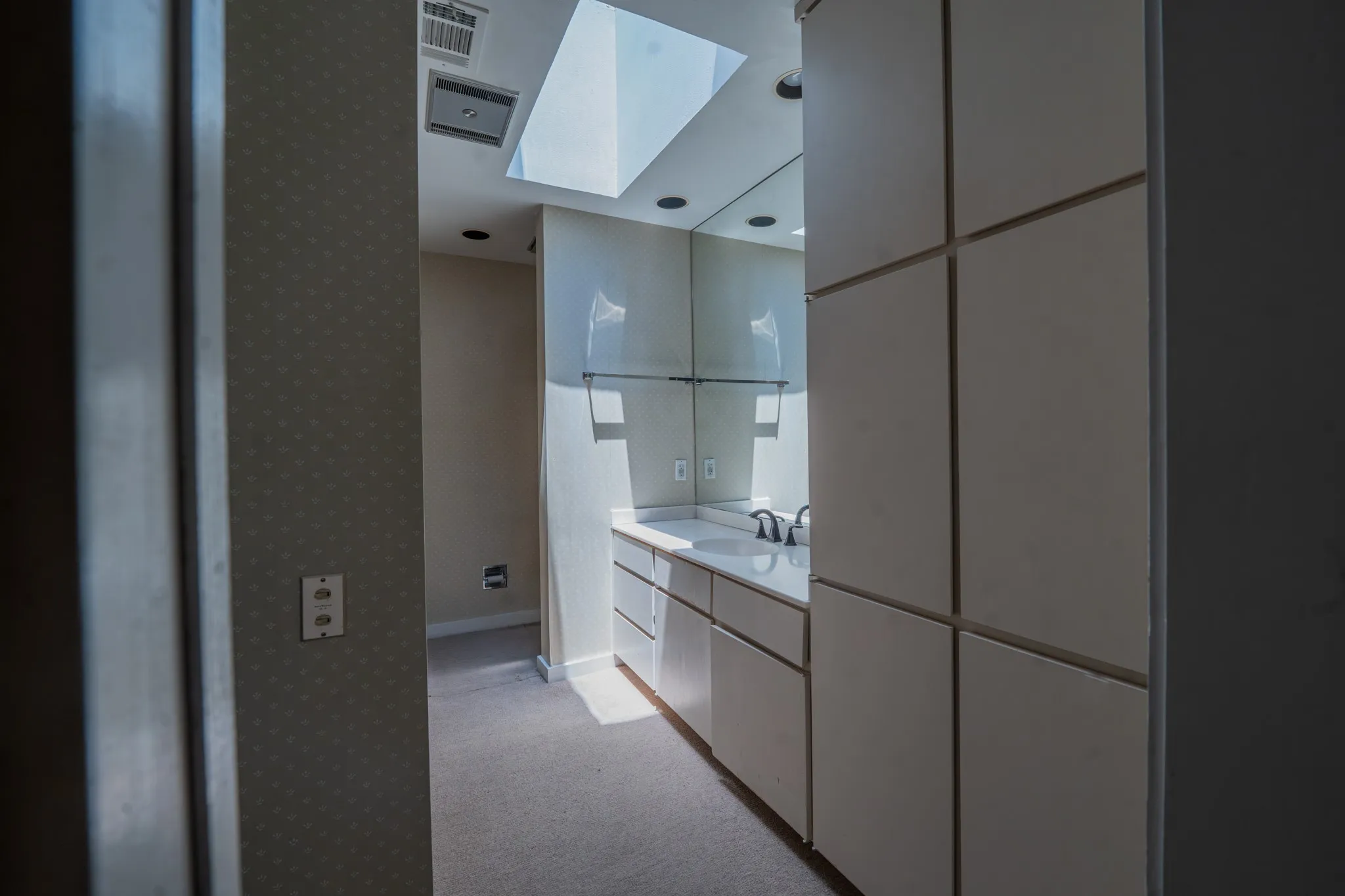Skylight-illuminated vanity space featuring an integrated sink, polished countertop, dark-finish faucet, and extensive built-in cabinetry