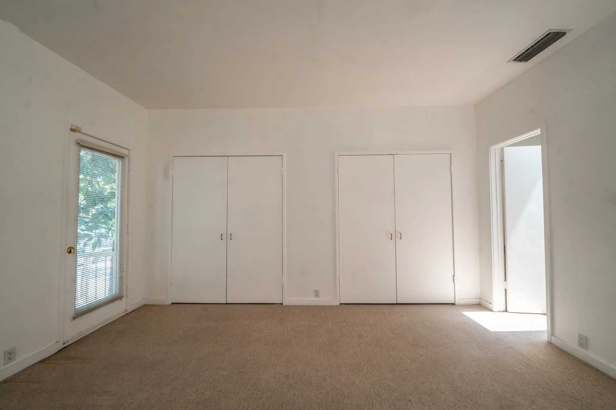 Carpeted room featuring a ceiling vent, two sets of bi-fold closet doors, a white baseboard trim, and a glass-paneled exterior door
