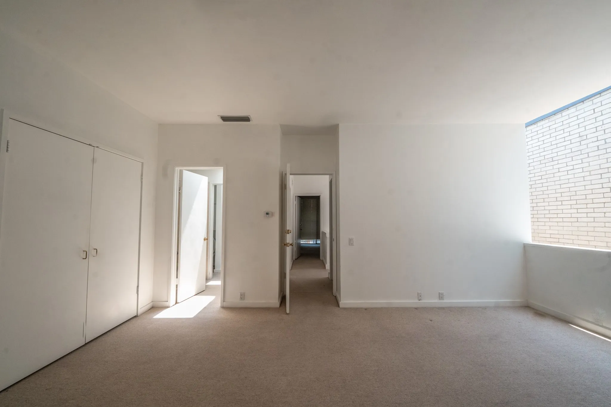 Spacious room featuring neutral carpeting, white walls, two bi-fold closet doors, and doorways to bathroom