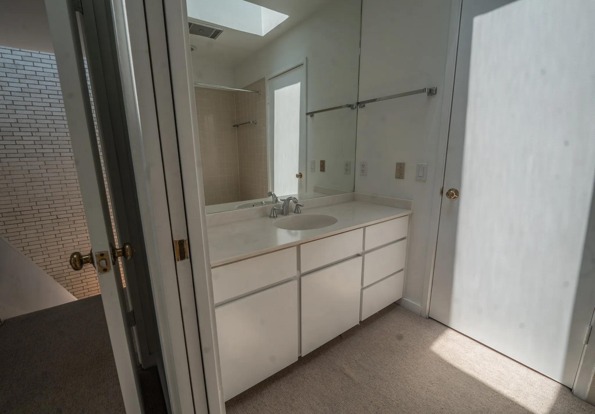 White vanity with an integrated sink and countertop, mirrored wall, recessed lighting, and a skylight