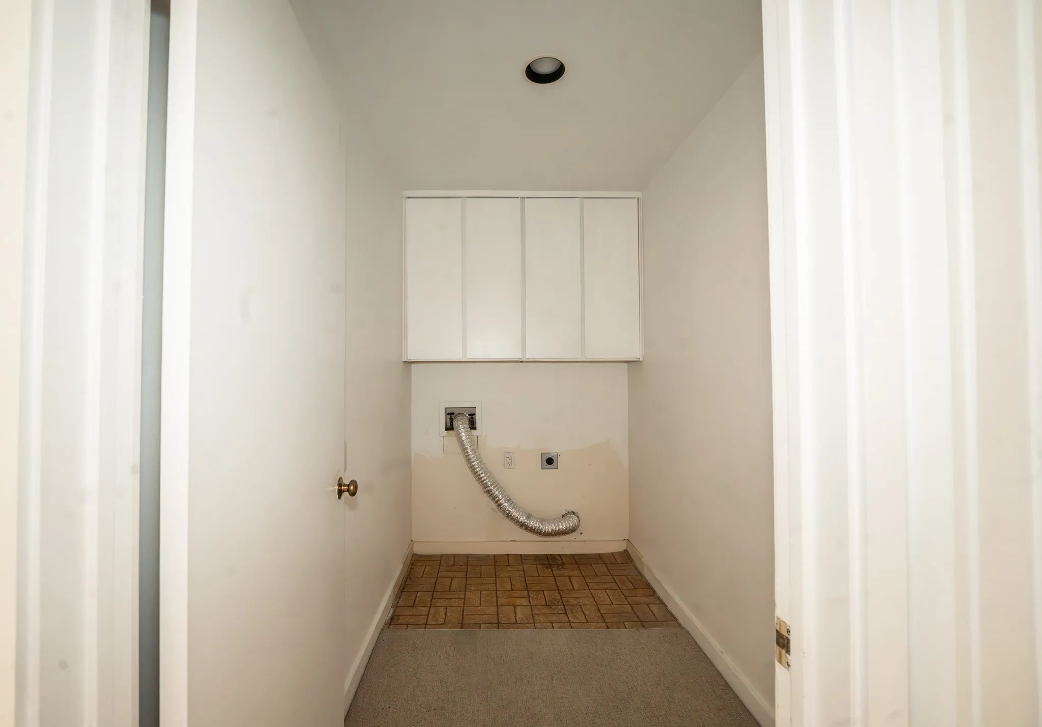 Dedicated laundry area featuring upper white cabinetry, a recessed ceiling light, and a combination of carpet and brown tile flooring