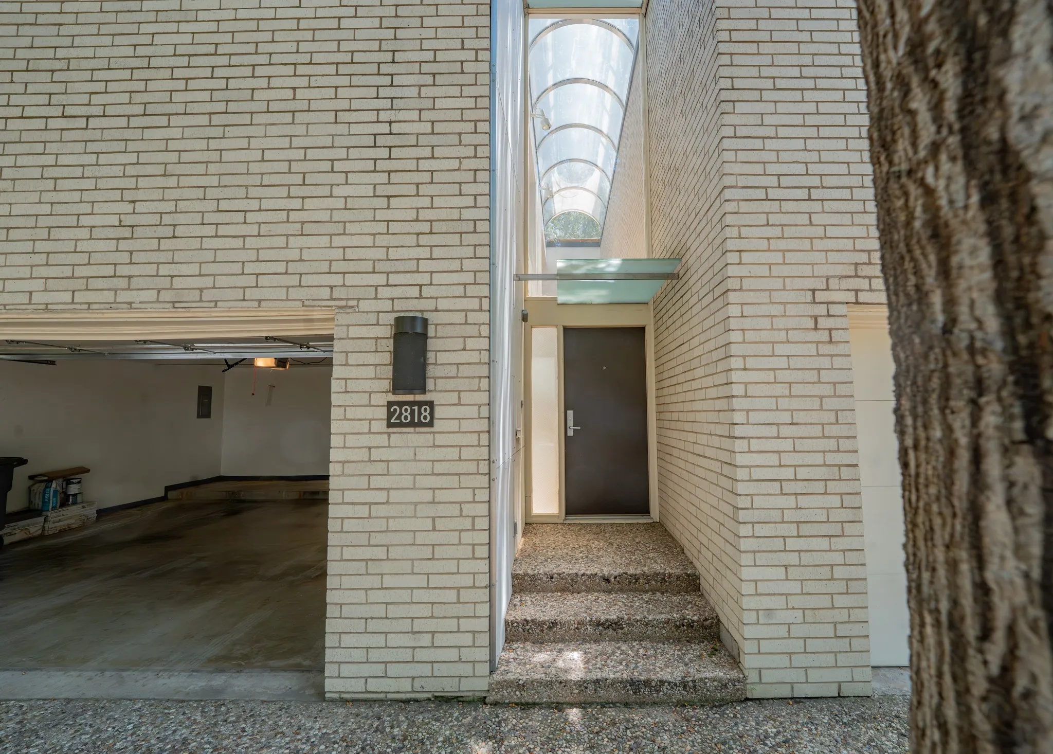 Light-colored brick exterior featuring an attached garage, modern front entry with an overhead glass canopy, and an arched skylight above the entry steps