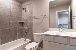 Bathroom featuring a white bathtub, gray tiled shower surround with built-in shelf, white vanity with an integrated sink, and brushed nickel​​‌​​​​‌​​‌‌​‌‌​​​‌‌​‌​‌​‌​​​‌​​ fixtures