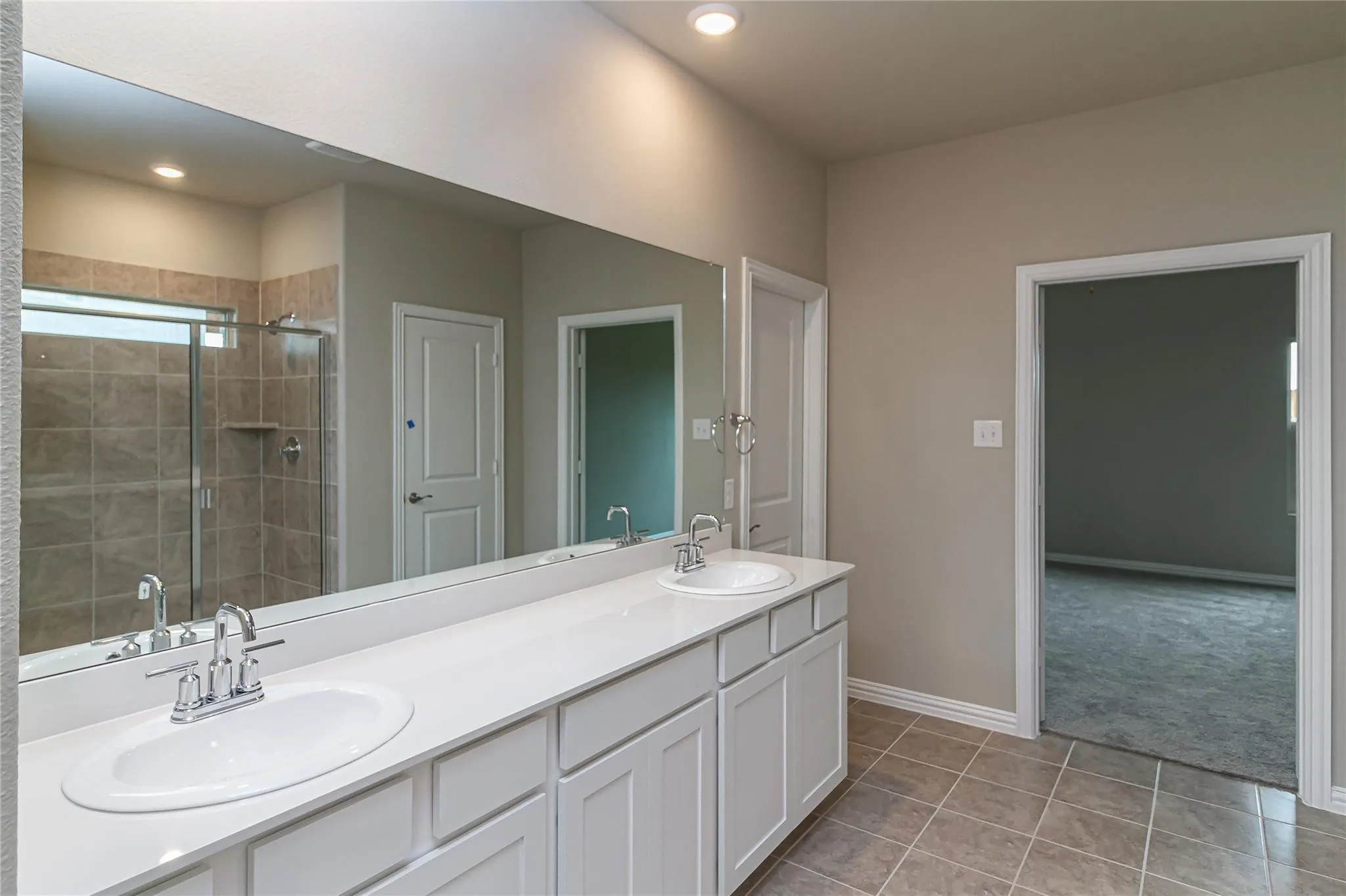 Dual vanity with white cabinetry, integrated sinks, chrome faucets, and an expansive wall-mounted mirror