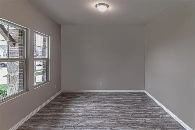 Interior room with two windows, wood-finish flooring, neutral gray wall paint, white trim, and a flush-mount ceiling light fixture