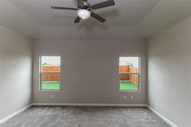 Spacious room featuring a tray ceiling with a ceiling fan and light fixture, two windows, gray carpeting, and white baseboards
