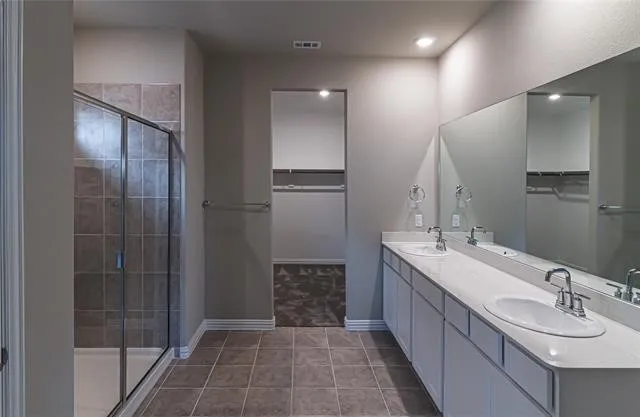 Bathroom featuring a dual vanity with white cabinetry and integrated sinks, a large wall-mounted mirror, recessed lighting, and a walk-in shower with tile surround and glass enclosure