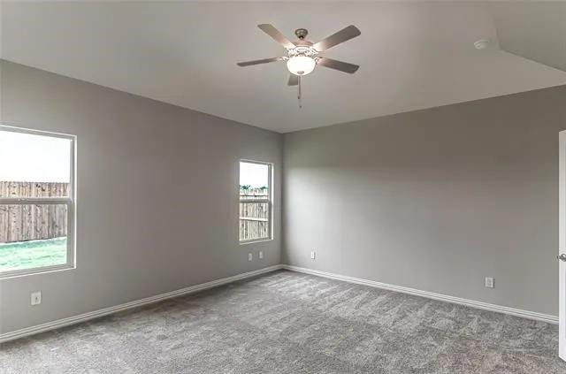 Spacious room featuring vaulted ceilings, a ceiling fan with integrated lighting, two windows, and textured gray carpeting
