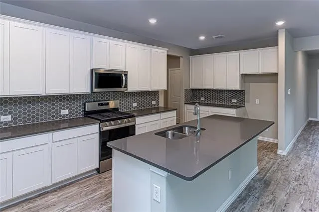Modern kitchen featuring a central island with an undermount double sink, gray countertop, and contemporary faucet