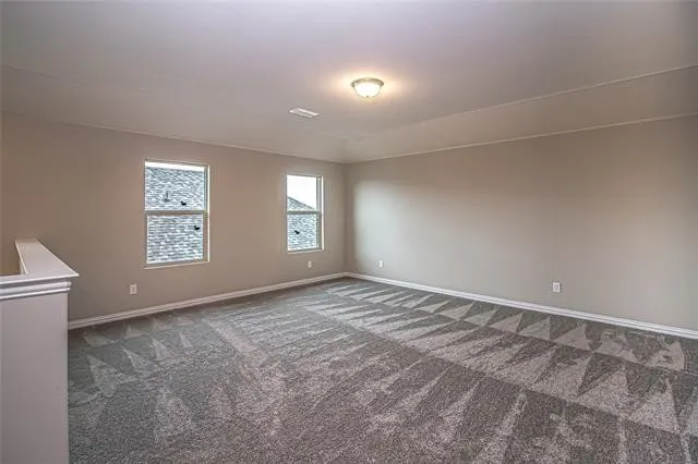 Spacious room featuring neutral paint, patterned carpeting, white baseboards, and two windows