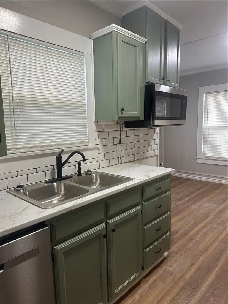 Kitchen featuring sage green cabinetry, white countertops, subway tile backsplash, stainless steel double basin sink with a black faucet, and wood-finish flooring