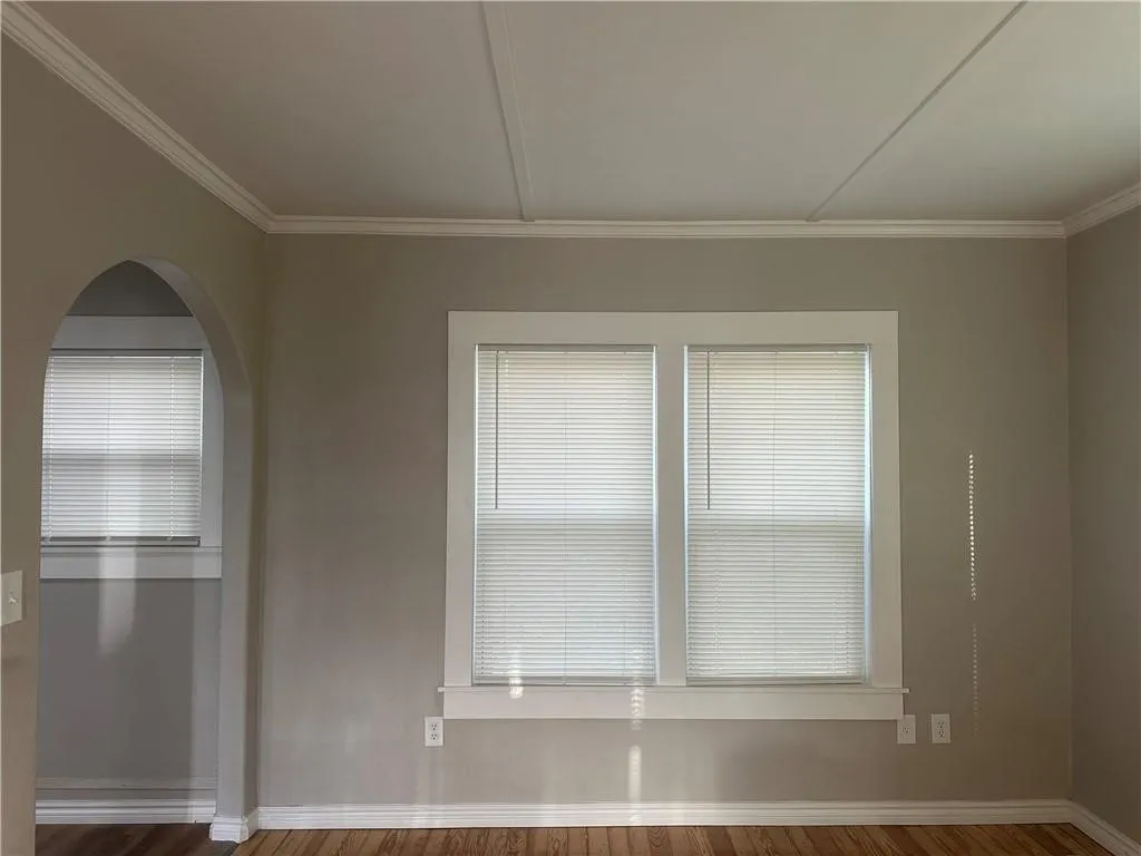 Hardwood flooring throughout, featuring a double window with blinds and an arched doorway