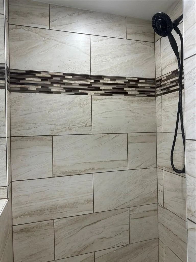 Tiled shower enclosure featuring a dark-finish shower head and mosaic accent band