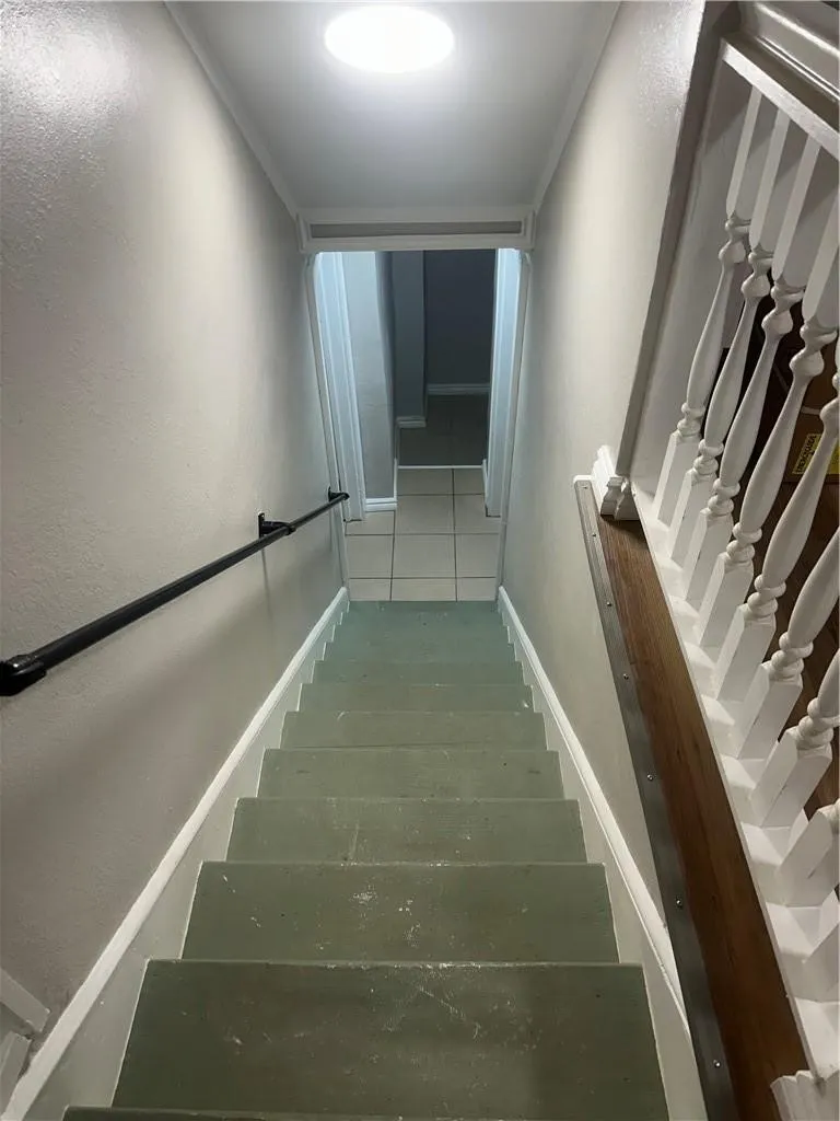 Staircase featuring a round ceiling light fixture, black wall-mounted handrail, and white painted balusters with a wood-finish handrail