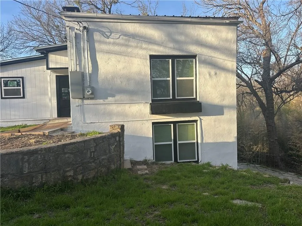 White stucco exterior featuring multiple windows with dark trim, a stone retaining wall, and a black exterior door