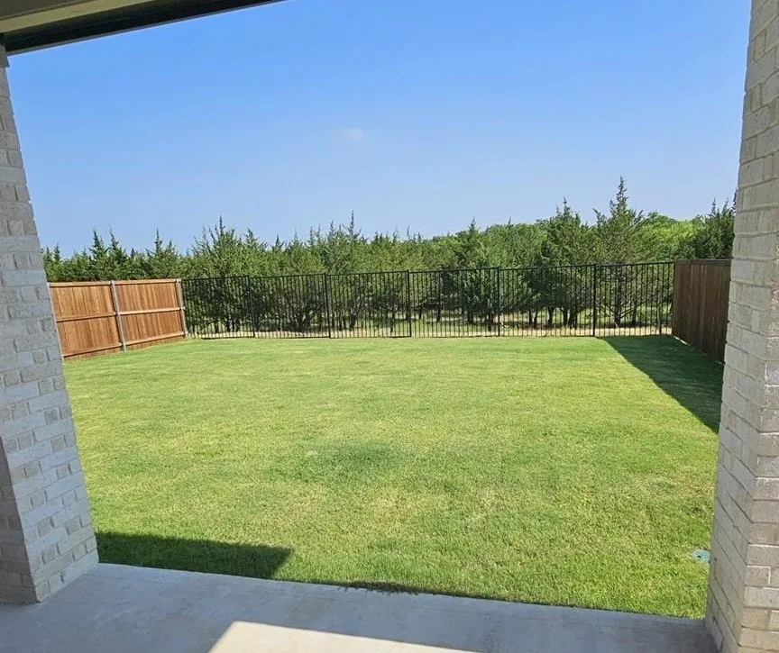 Expansive rear yard featuring a manicured lawn and a combination of wood and wrought iron fencing