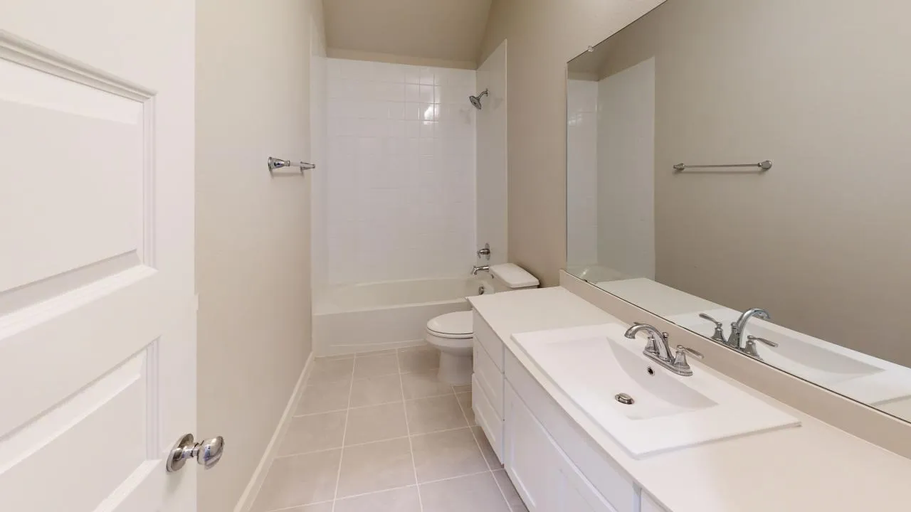 Bathroom featuring a white vanity with an integrated sink, polished chrome faucet, a large wall-mounted mirror, a white bathtub with a tiled shower surround, and neutral-toned tile flooring