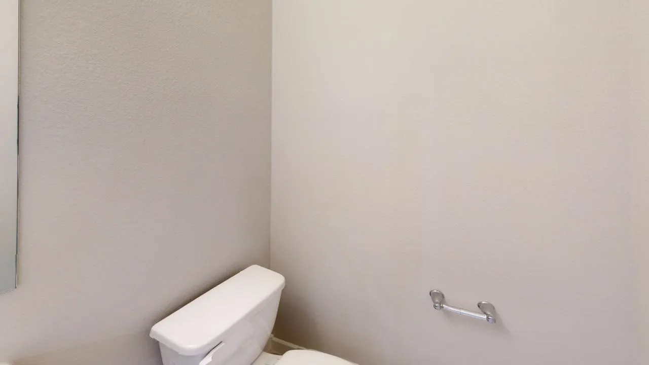 White toilet with a wall-mounted chrome toilet paper holder and a partially visible mirror