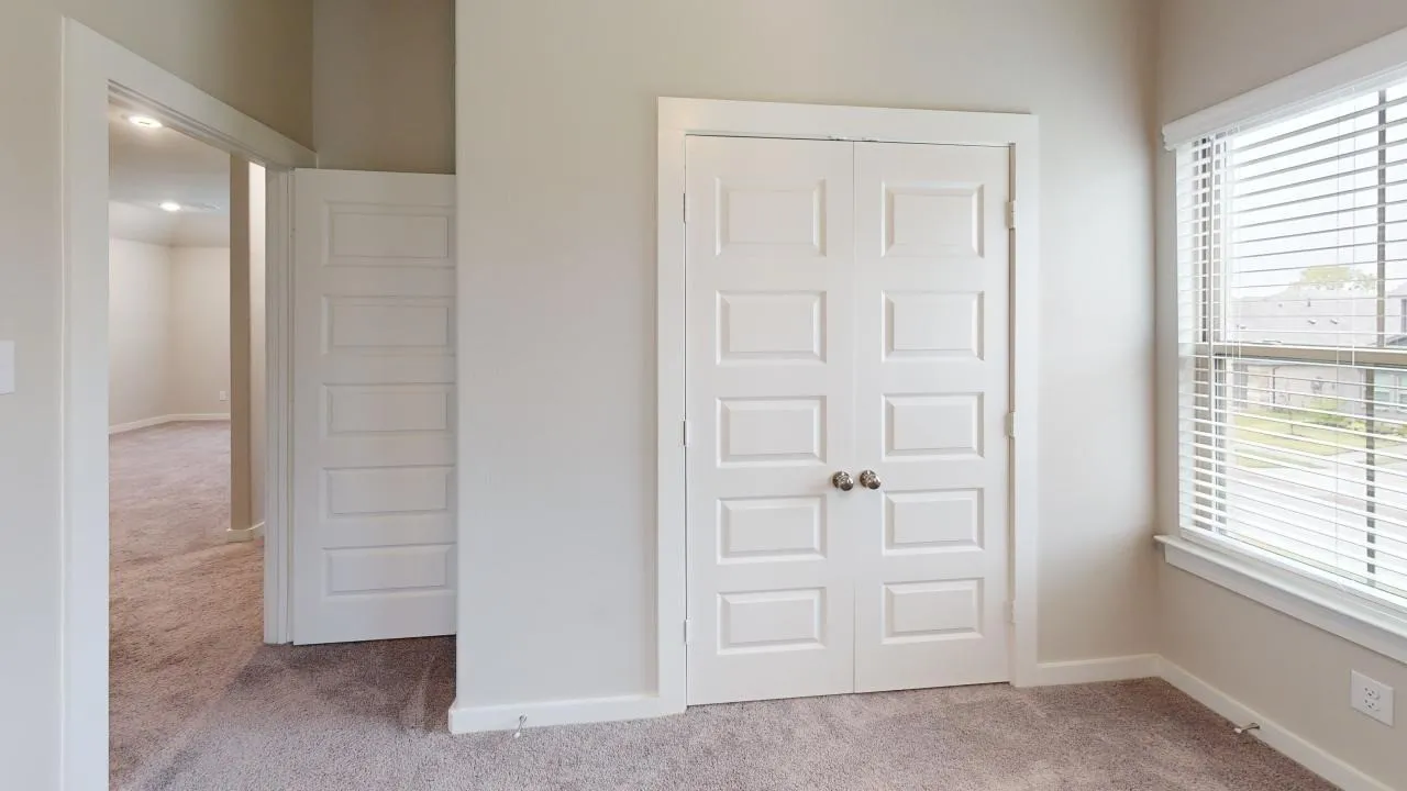 Neutral-toned room with plush carpet flooring, featuring a window with white blinds and white trim
