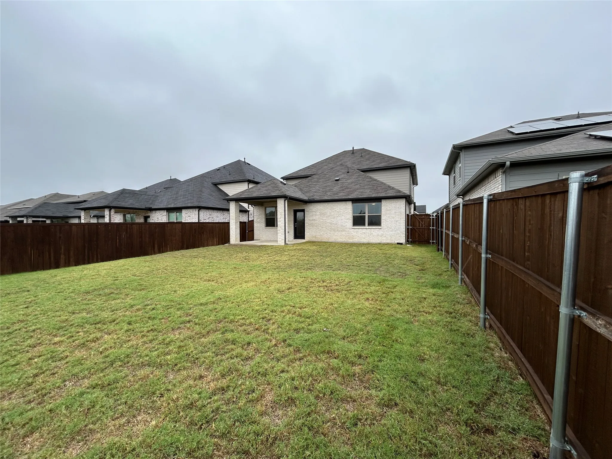 Expansive backyard featuring a manicured lawn, full privacy fencing, a covered patio, and light brick exterior
