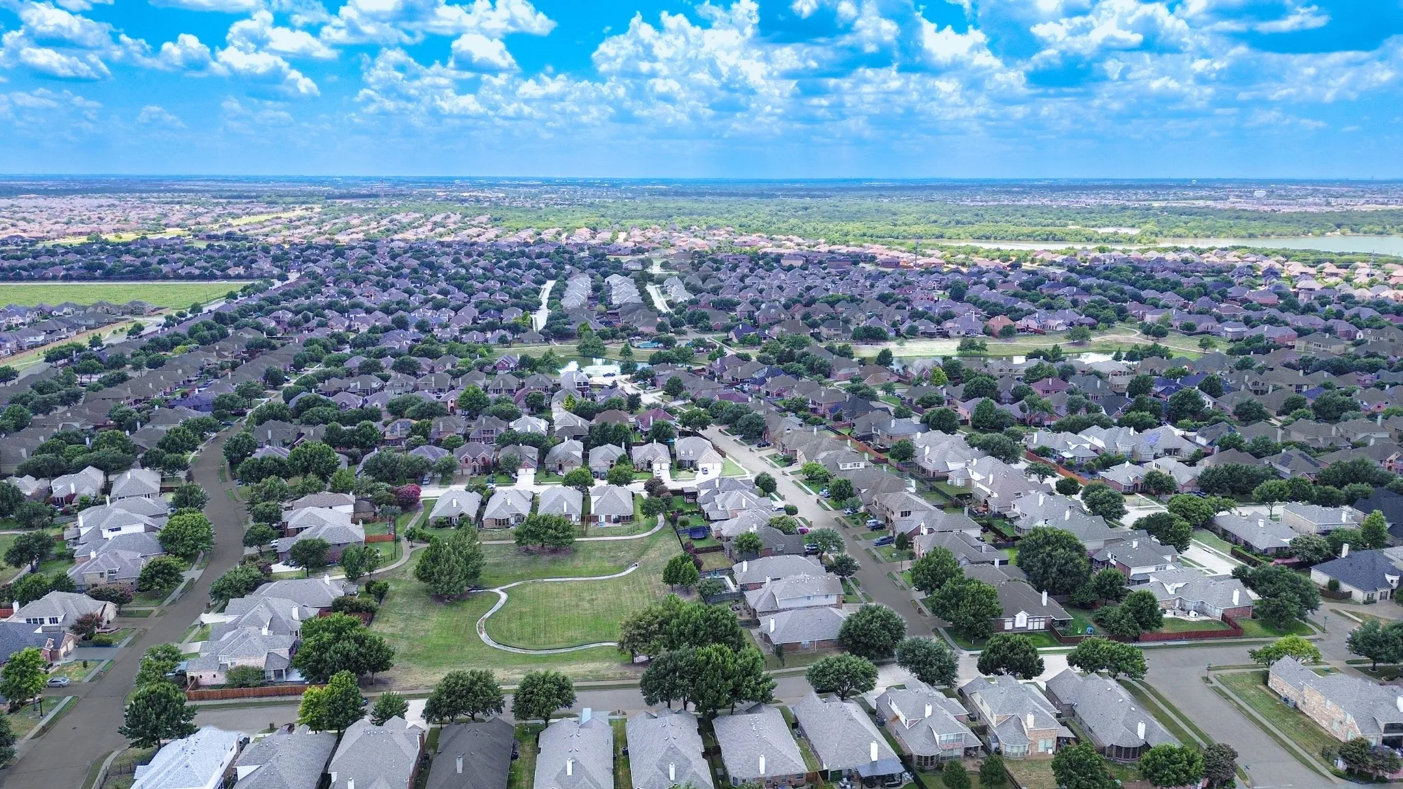 Aerial view of a residential neighborhood with numerous single-family homes, mature trees, and a distant body of water