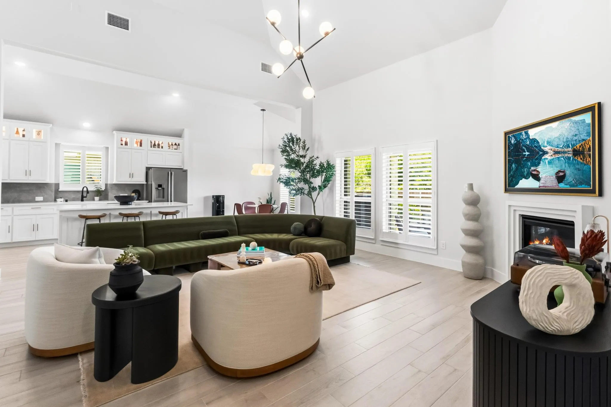 Spacious open-concept living area featuring high vaulted ceilings, light wood-finish flooring, and a contemporary fireplace with a classic mantel