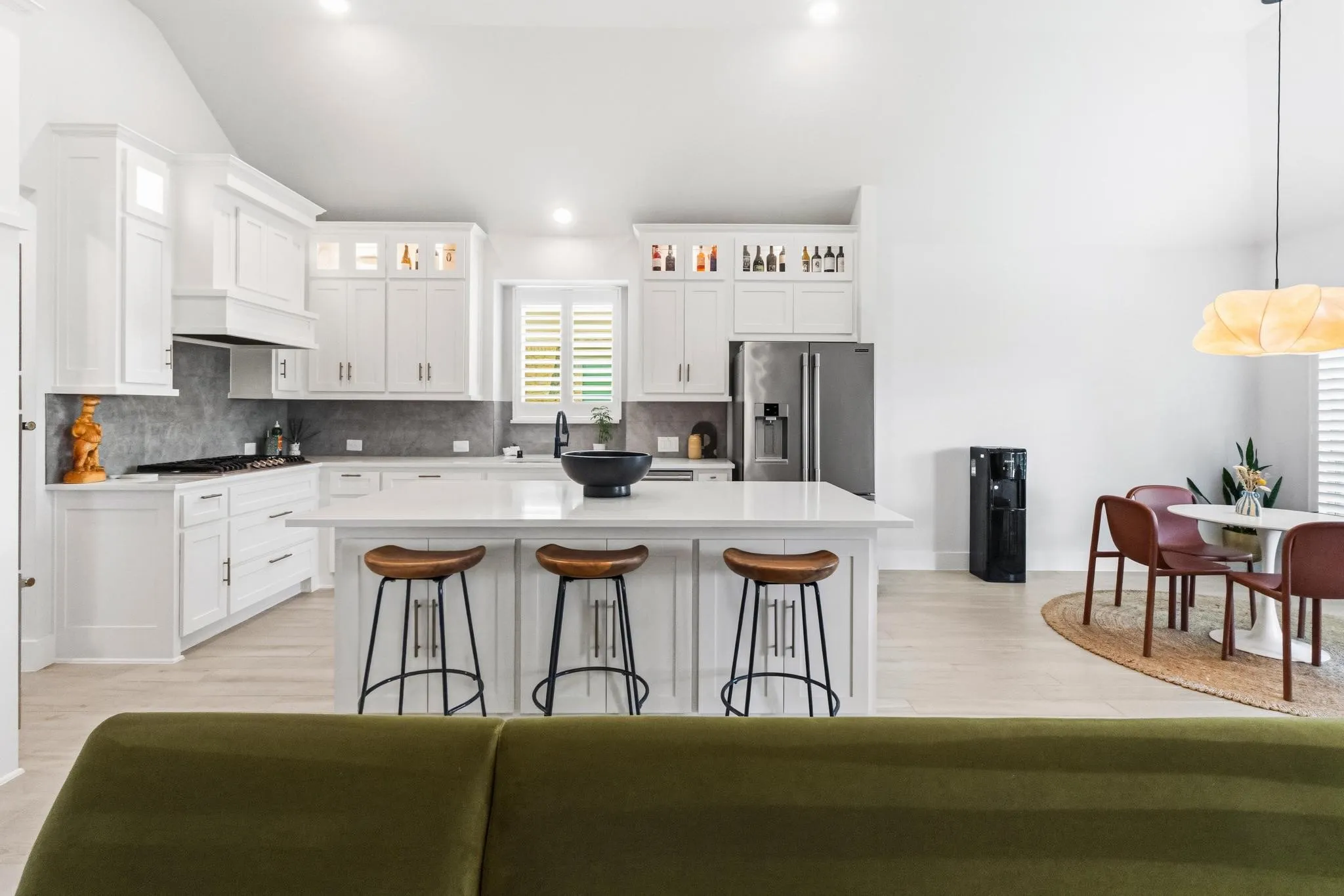Spacious kitchen featuring white cabinetry, a large center island with seating, stainless steel appliances, and a gray tile backsplash