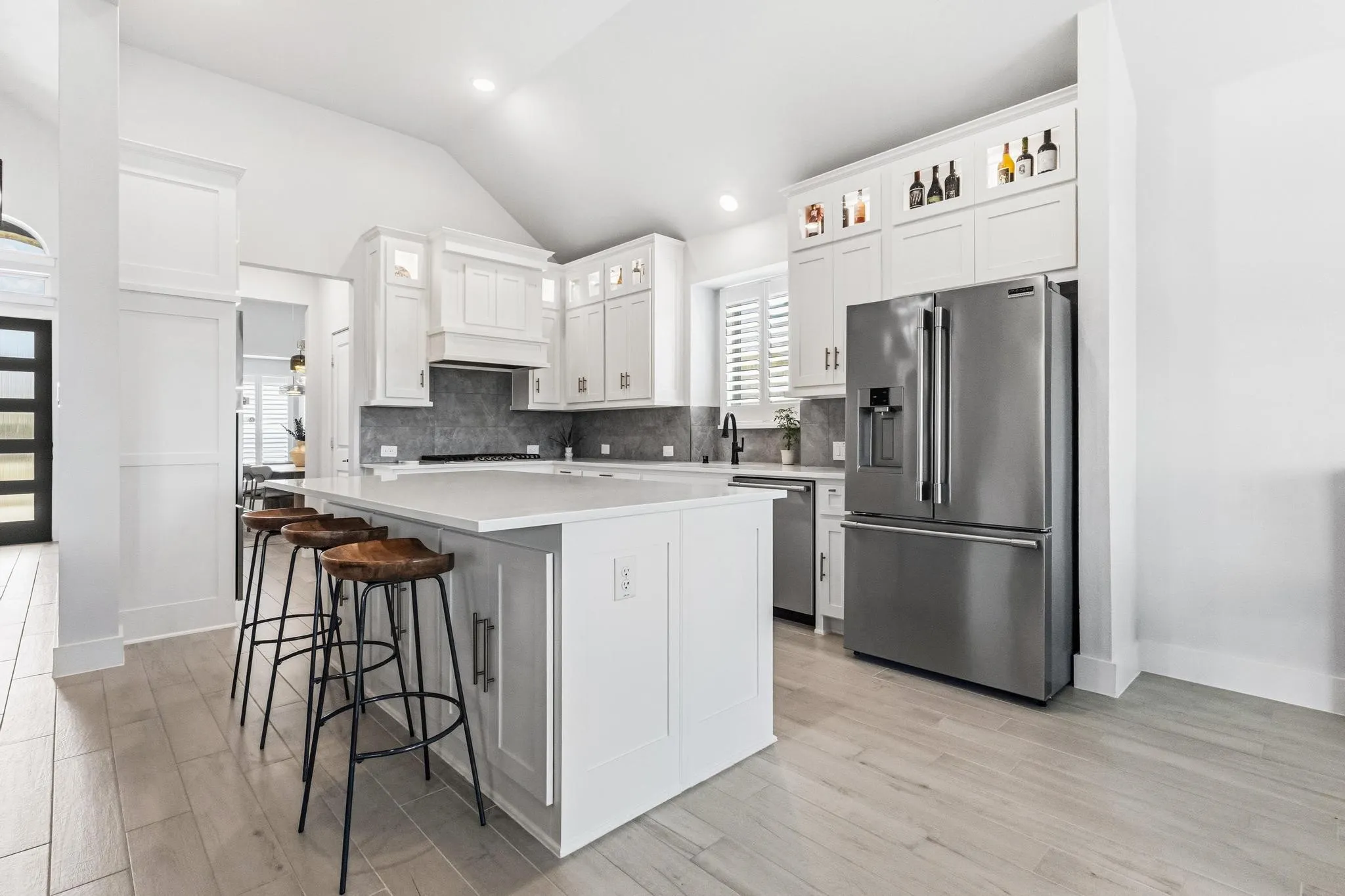 Open-concept kitchen featuring an island with counter seating, light wood-finish flooring, white cabinetry, stainless steel appliances, and a vaulted ceiling