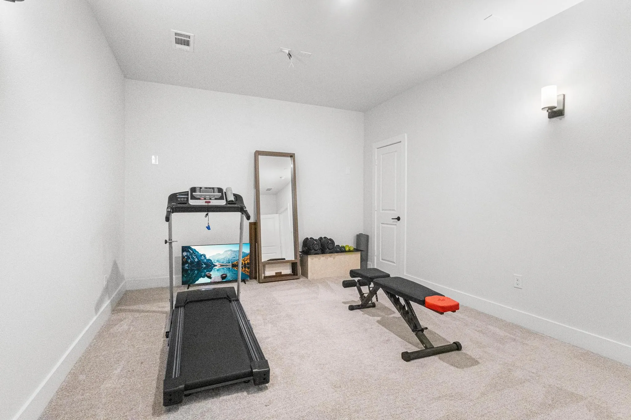 Versatile interior space featuring light-colored carpet flooring, white walls, and a contemporary wall sconce