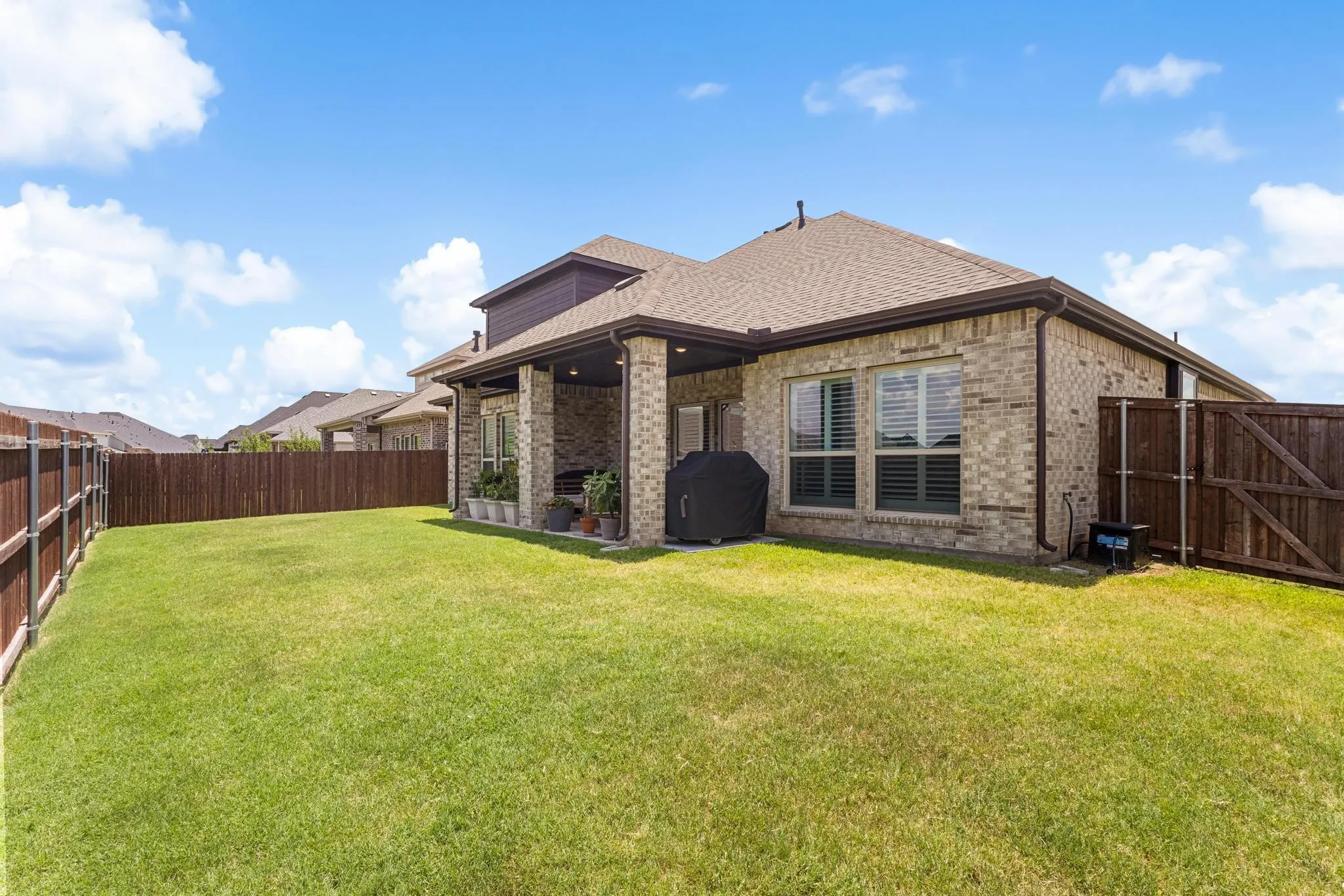 Expansive backyard featuring a manicured lawn, full privacy fencing, a covered patio, and brick exterior