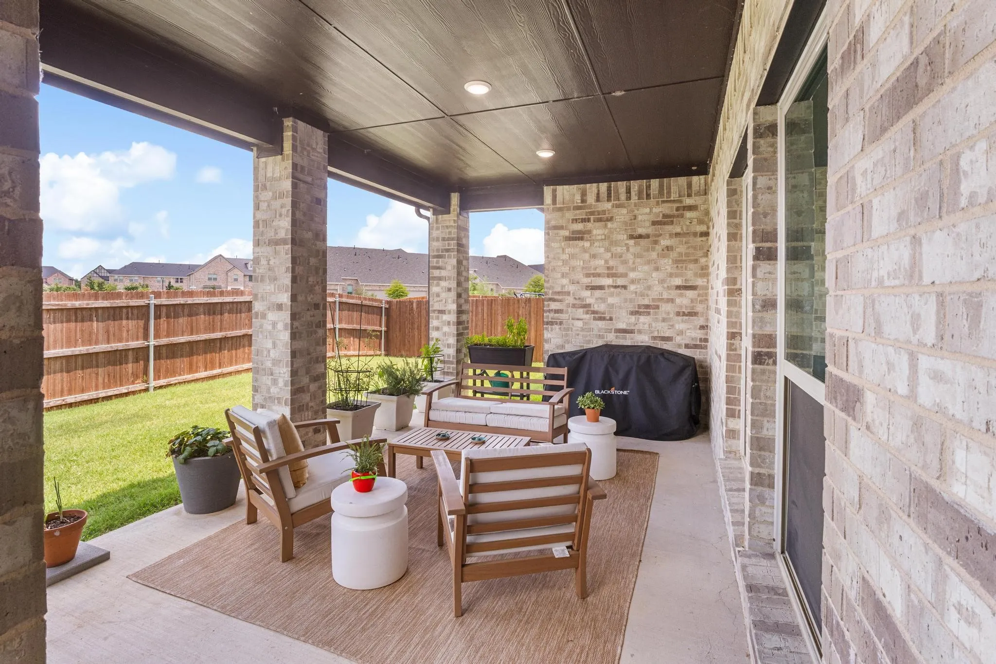 Covered concrete patio featuring recessed lighting, a light-toned brick exterior, and a fenced backyard with a manicured lawn