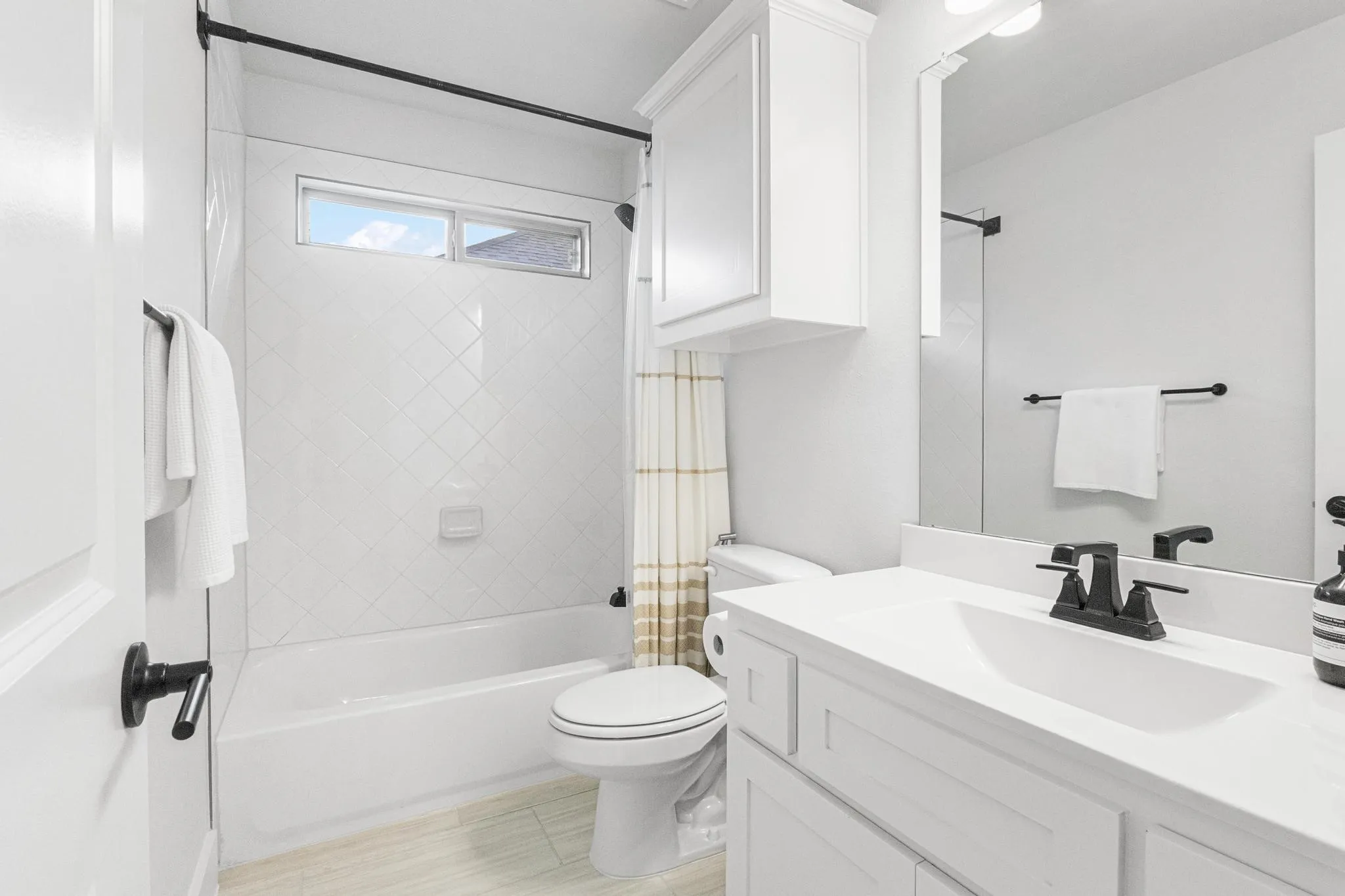White bathroom vanity with a single sink, black faucet, and white countertop