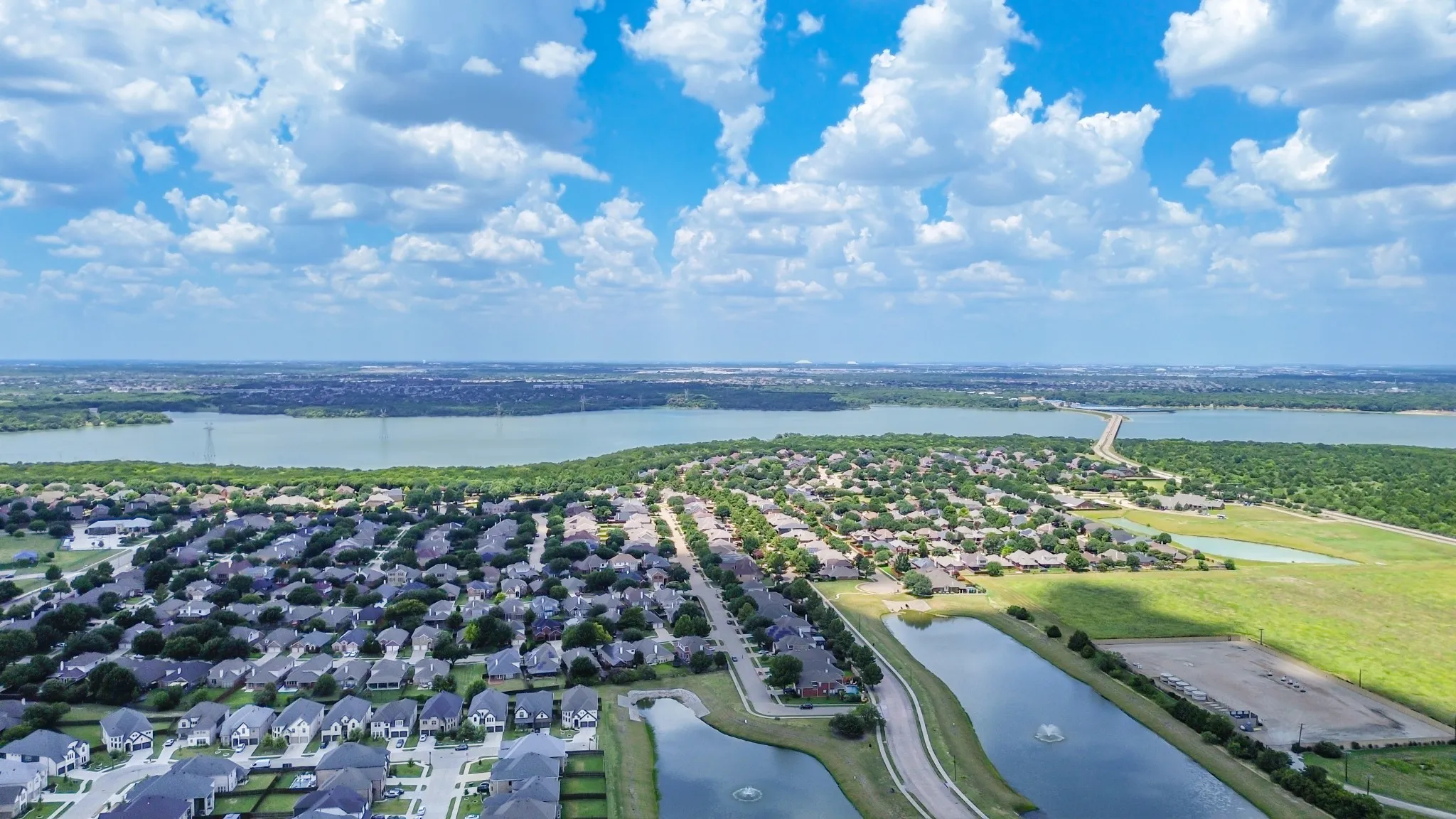Extensive residential development featuring numerous single-family homes, multiple retention ponds with aerators, and a large body of water in the background