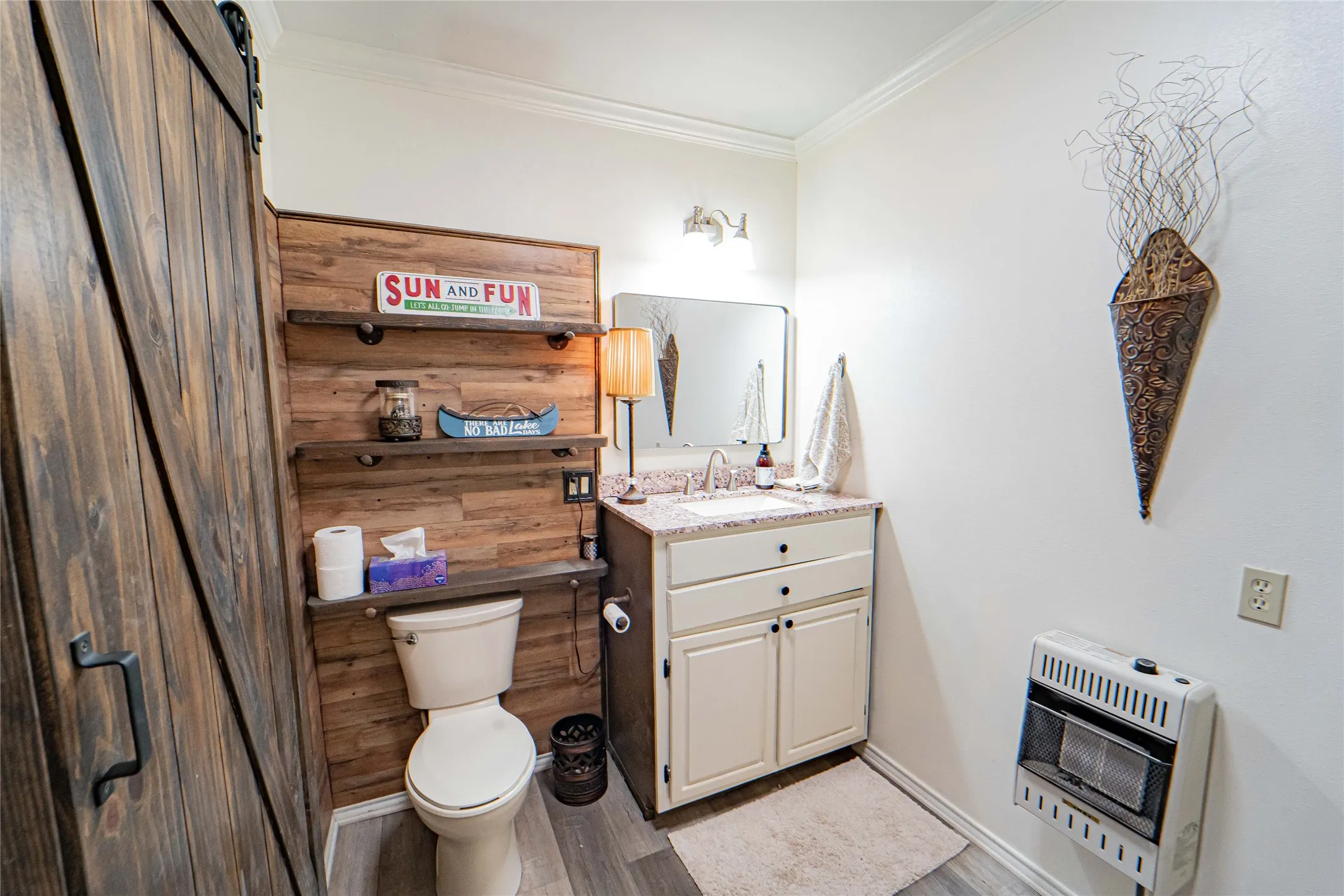 Barn door entry to a bathroom featuring a wood-plank accent wall with built-in shelving, a single vanity with a solid surface countertop, and wood-finish flooring
