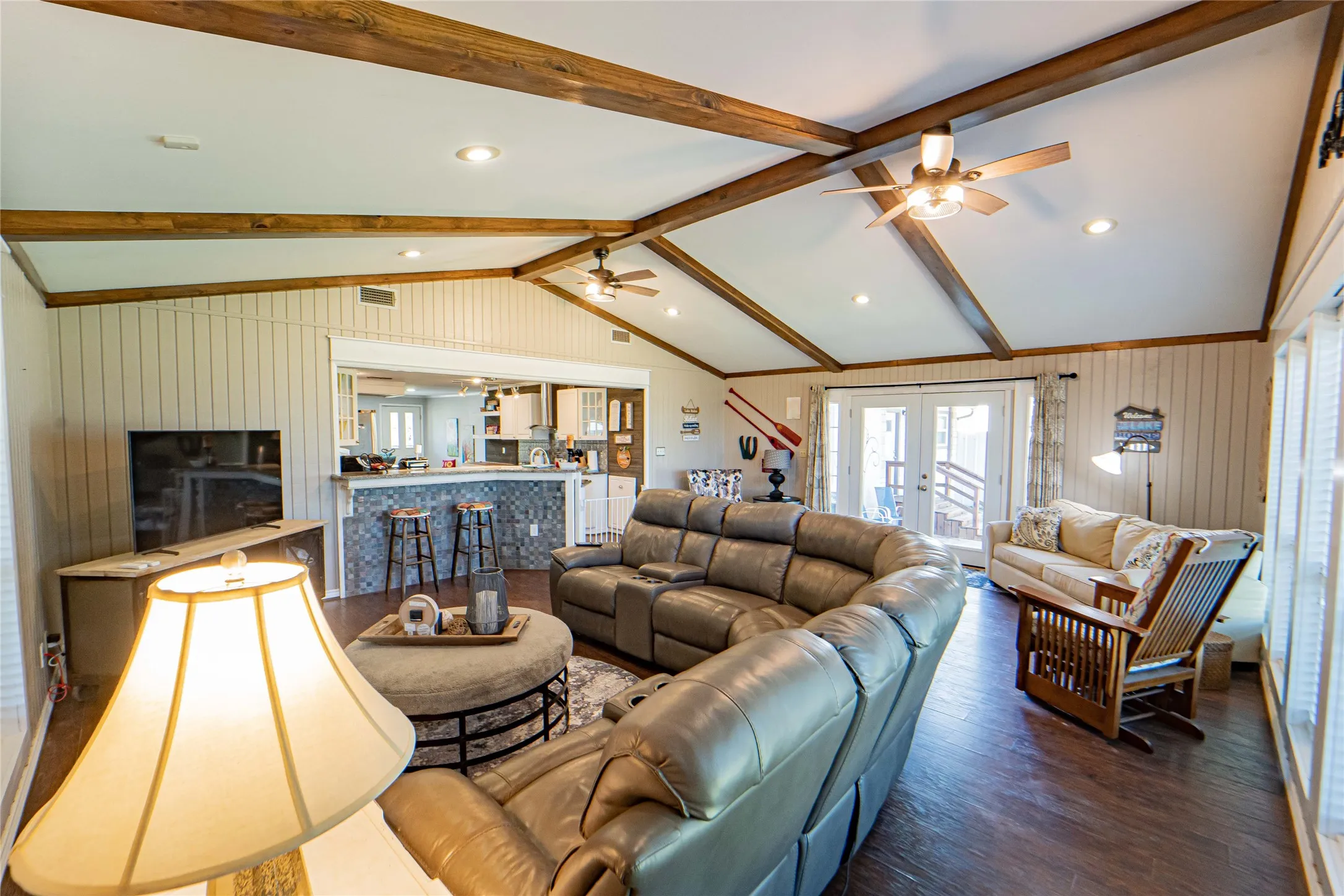 Cozy living area open to the kitchen with glass patio doors leading to the outdoors-Vaulted ceilings with exposed wood beams define this living area, featuring recessed lighting and ceiling fans
