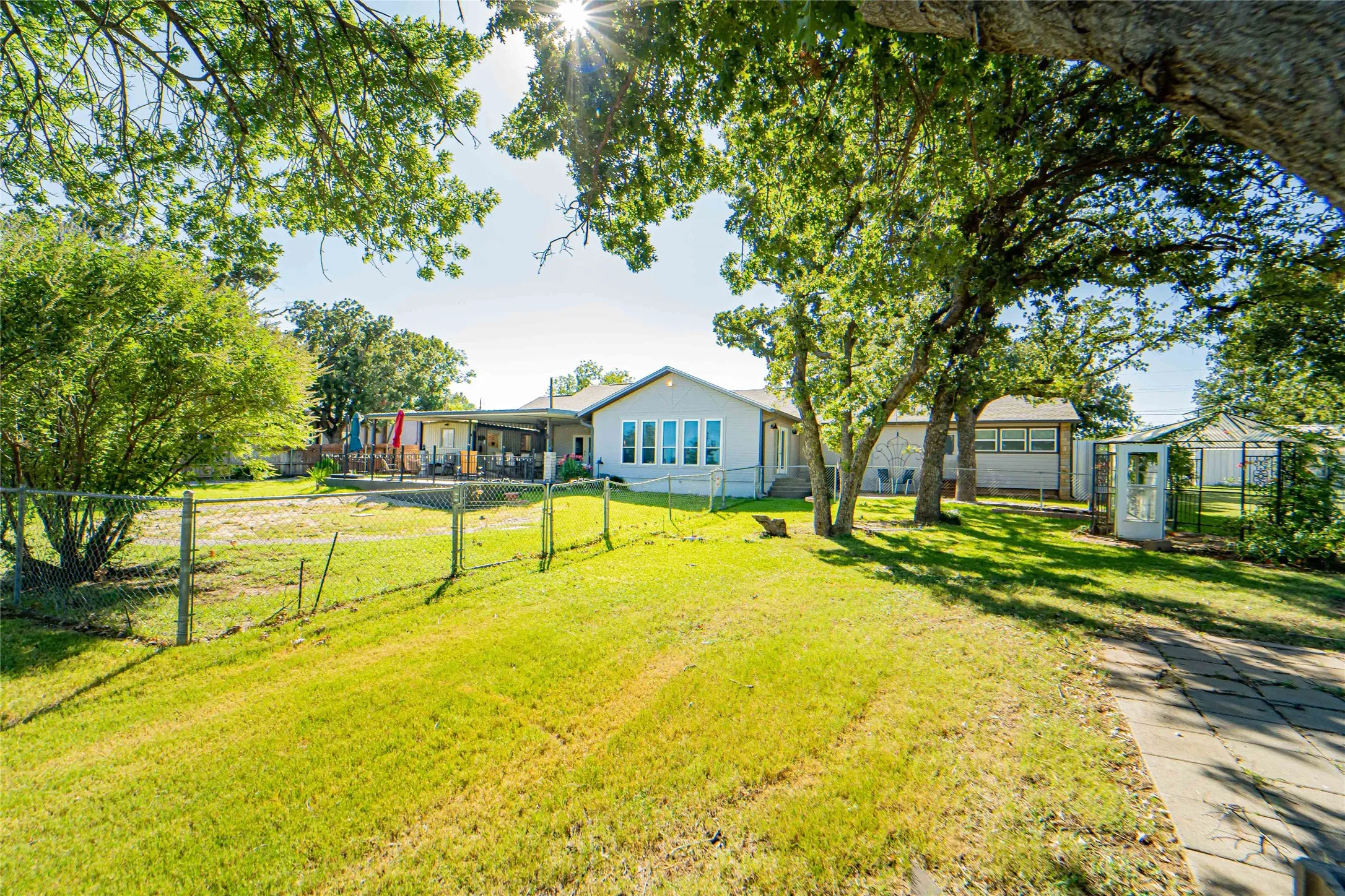 Expansive rear yard with a covered patio area, mature trees, a stone pathway, a fenced section, and an additional structure