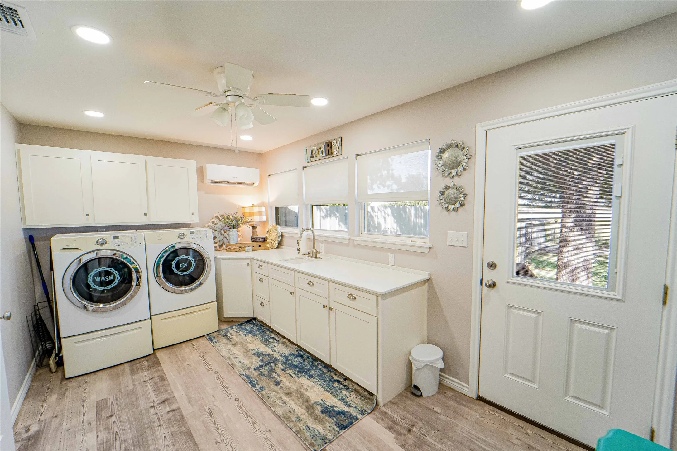 Dedicated laundry room featuring wood-finish flooring, white cabinetry, integrated sink with gooseneck faucet, and recessed lighting-great lakeside views and natural light