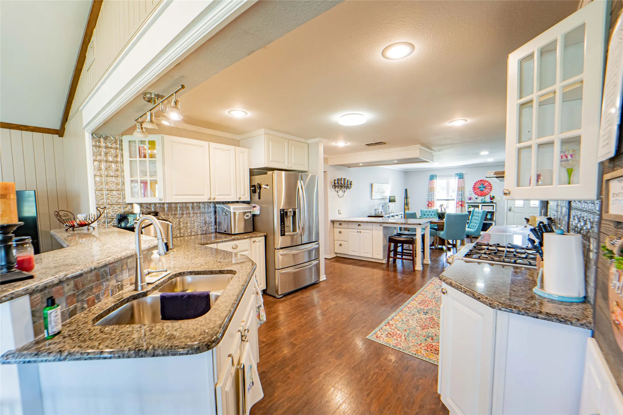 Updated Kitchen located centrally between living area and dining area,  featuring wood-finish flooring, recessed lighting, white cabinetry, a stainless steel double-door refrigerator, and granite countertops